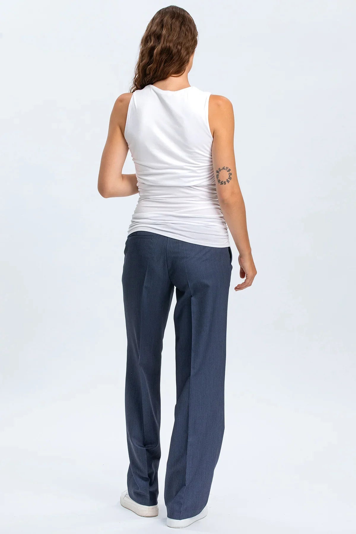 Modella vista da dietro con pantaloni premaman eleganti blu e top bianco senza maniche