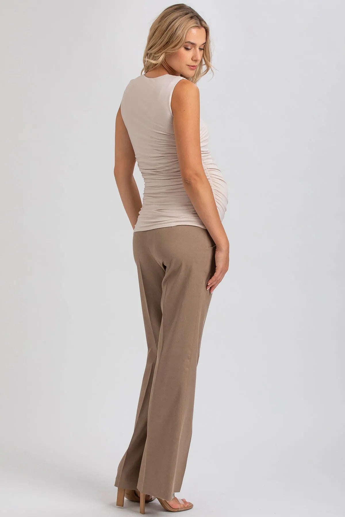 Donna incinta indossa top premaman beige senza maniche e pantaloni eleganti color sabbia.