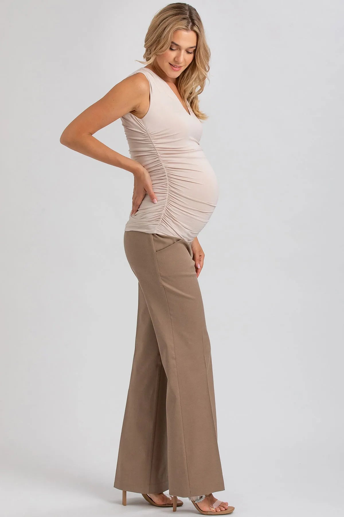 Donna in gravidanza con top premaman beige senza maniche e pantaloni larghi marroni