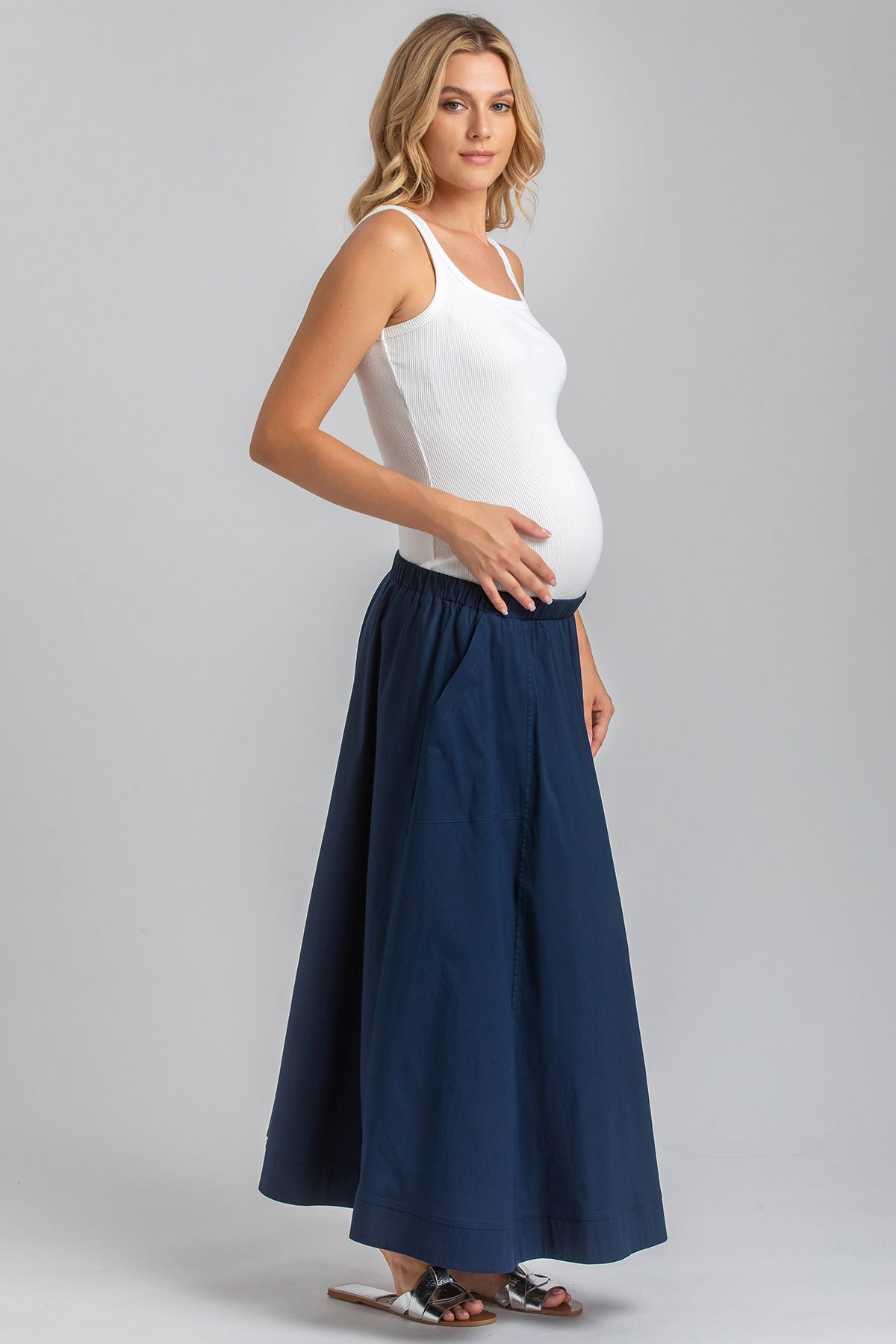 Donna incinta con top bianco e gonna blu, abbigliamento premaman elegante e confortevole