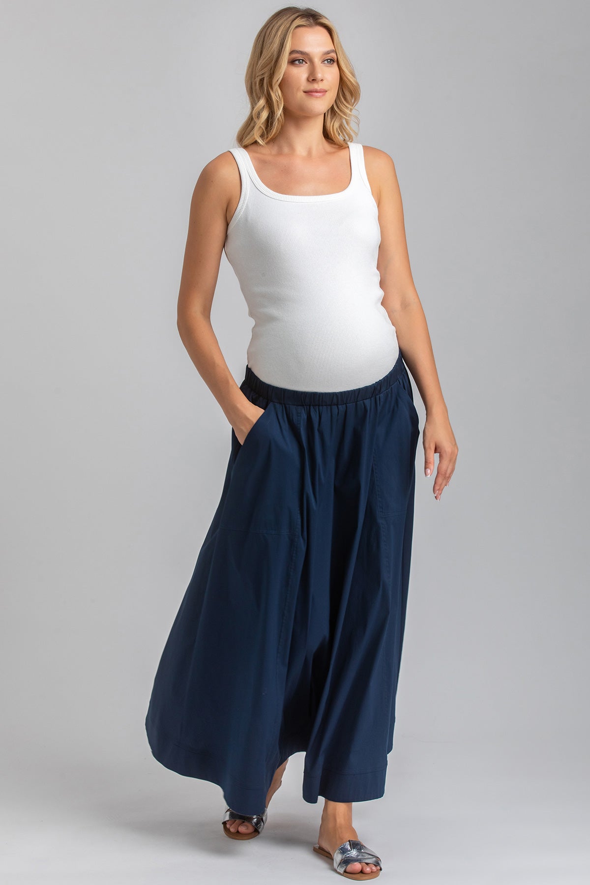 Donna incinta indossa top bianco e gonna lunga blu premaman, abbigliamento premaman elegante
