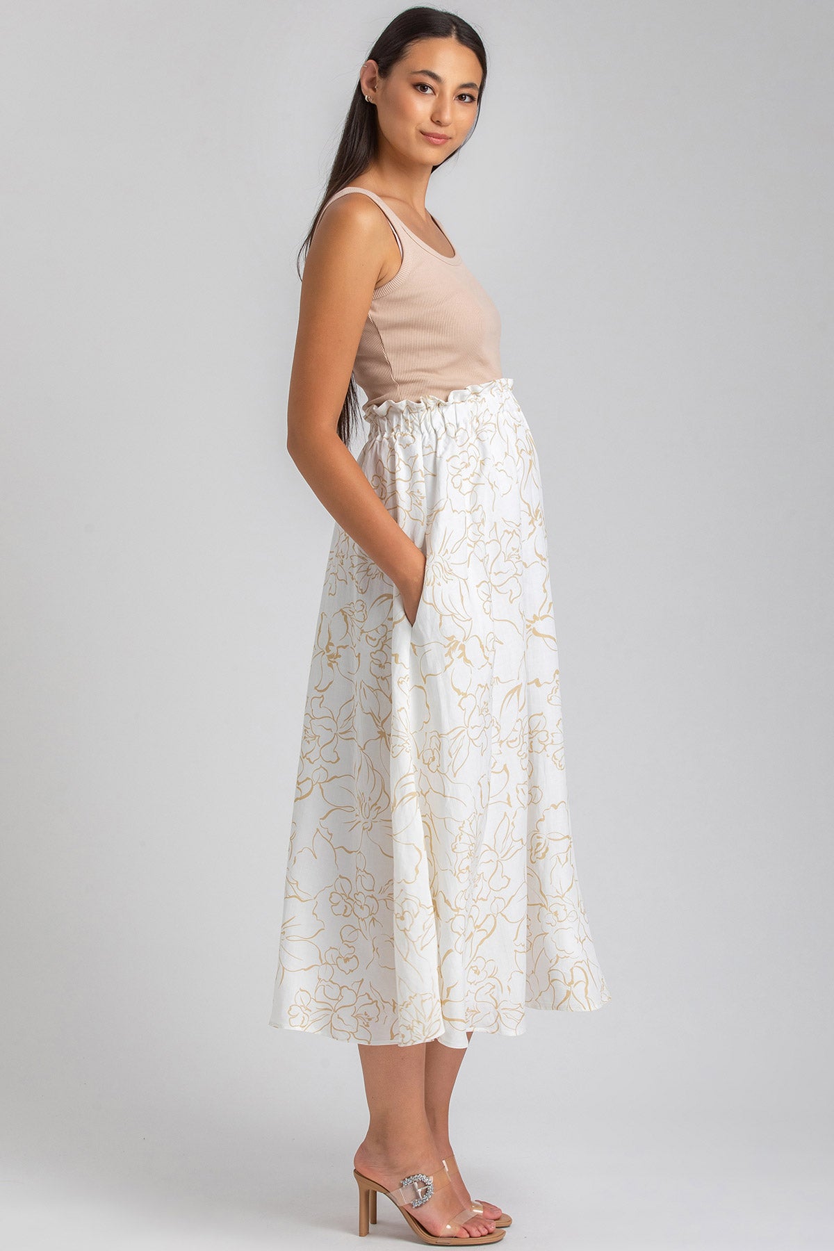 Donna incinta con gonna premaman bianca a fiori beige, top beige senza maniche, sandali trasparenti