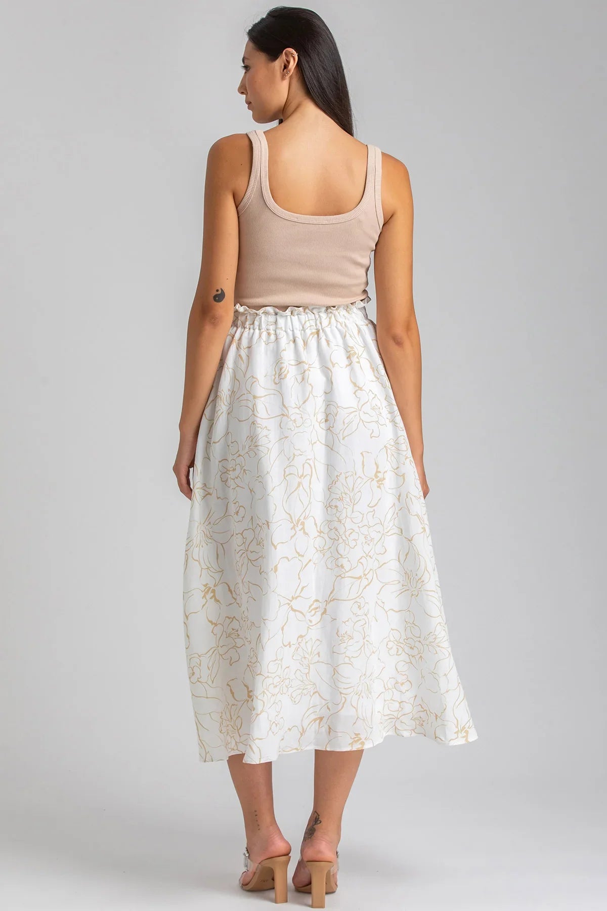 Donna di profilo con top beige e gonna lunga bianca premaman a fantasia floreale