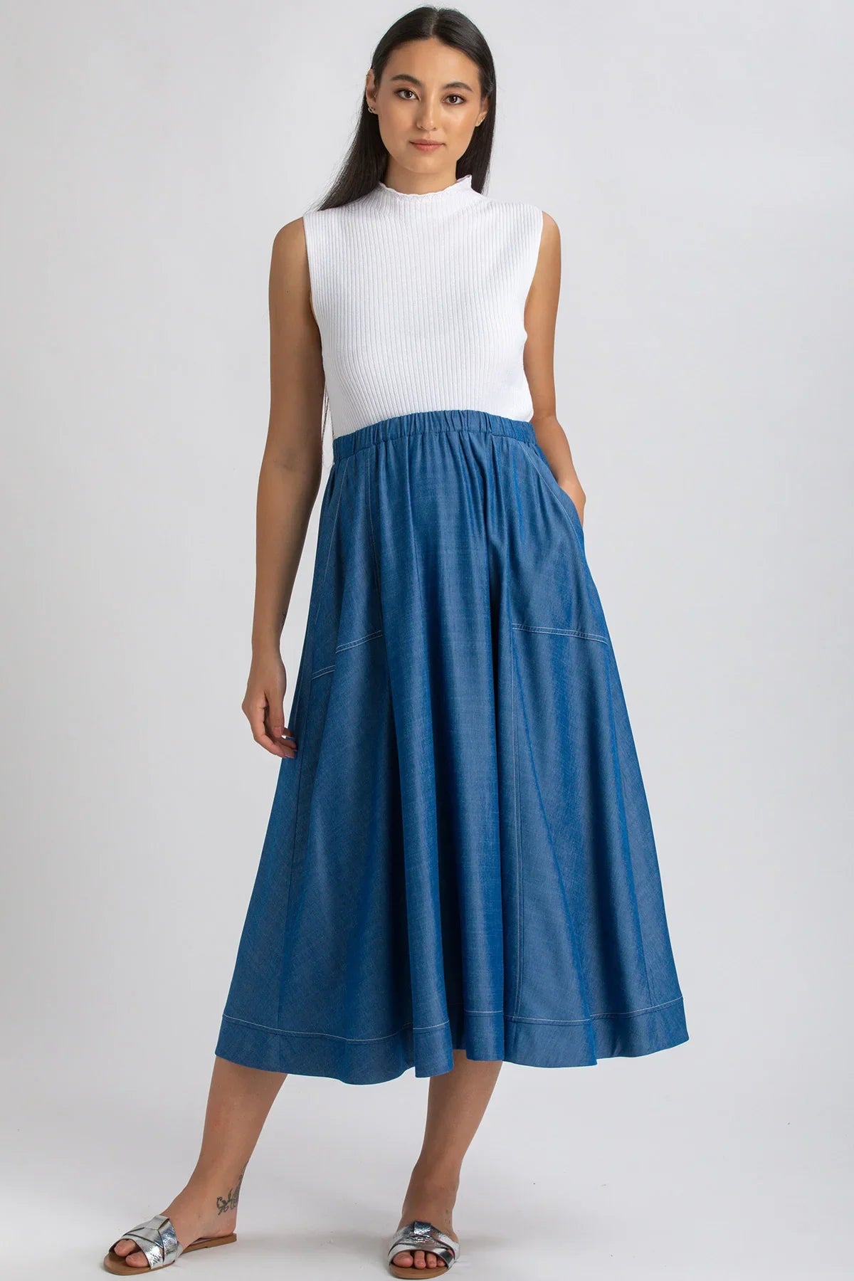 Donna con abito premaman smanicato bianco e gonna lunga blu, sandali flat, fondo neutro