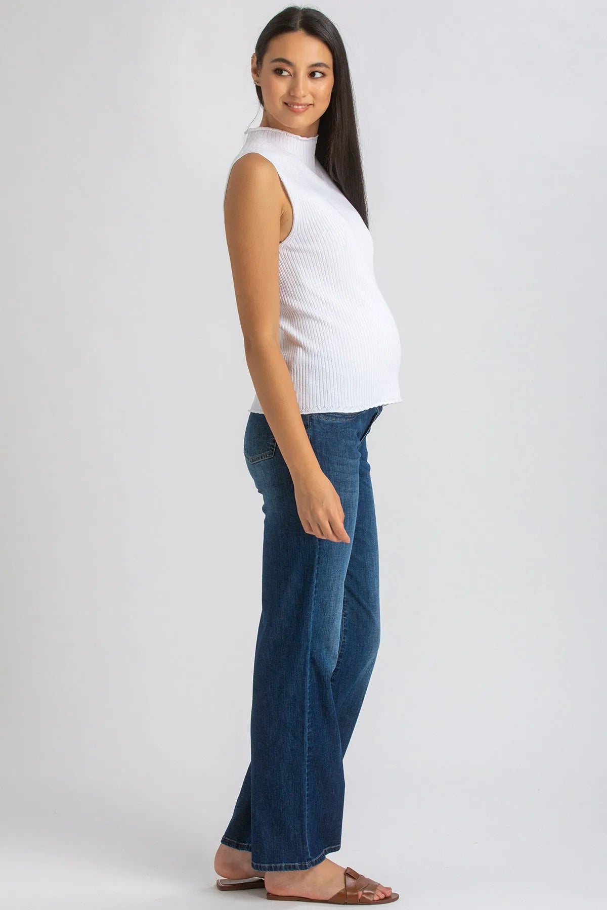 Modella incinta indossa top smanicato bianco e jeans premaman in denim blu