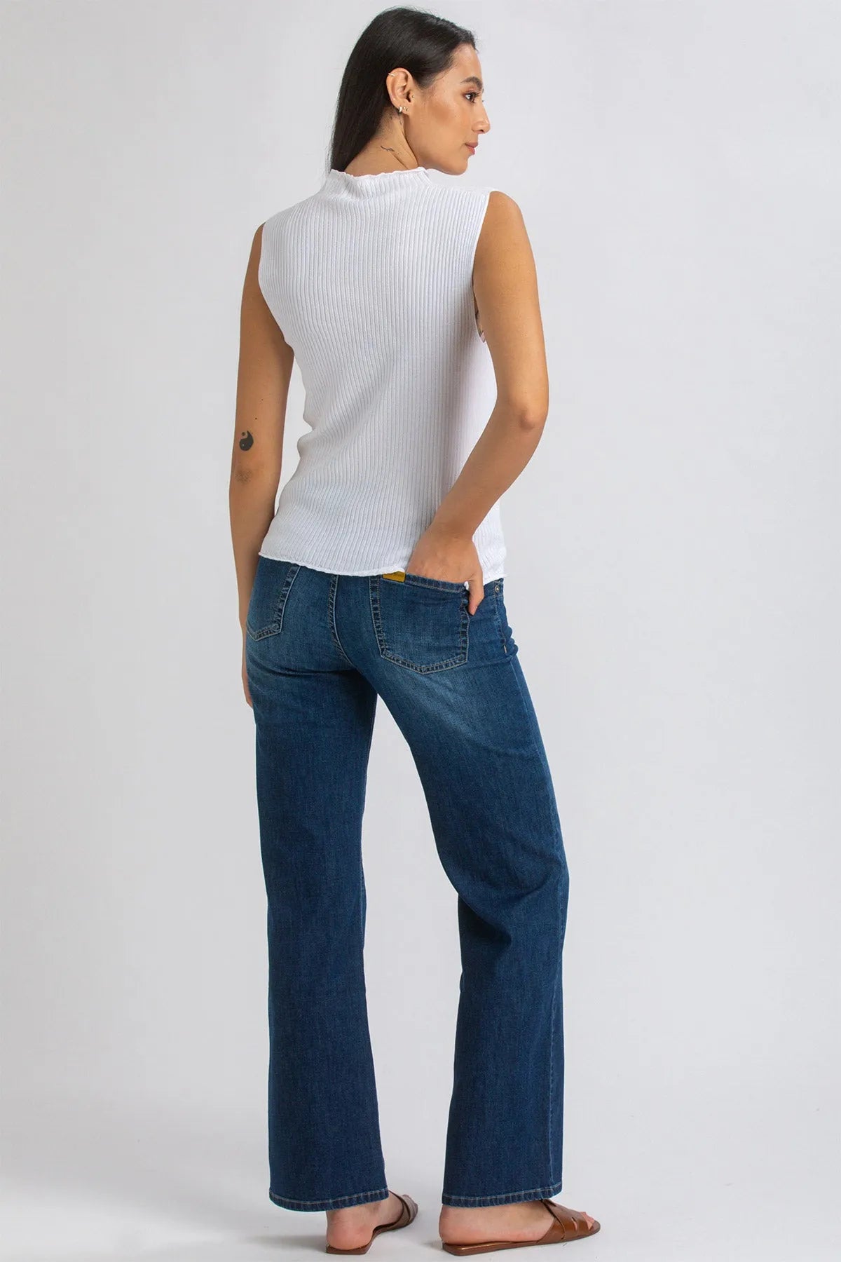 Donna con top senza maniche bianco e jeans premaman a zampa, vista posteriore