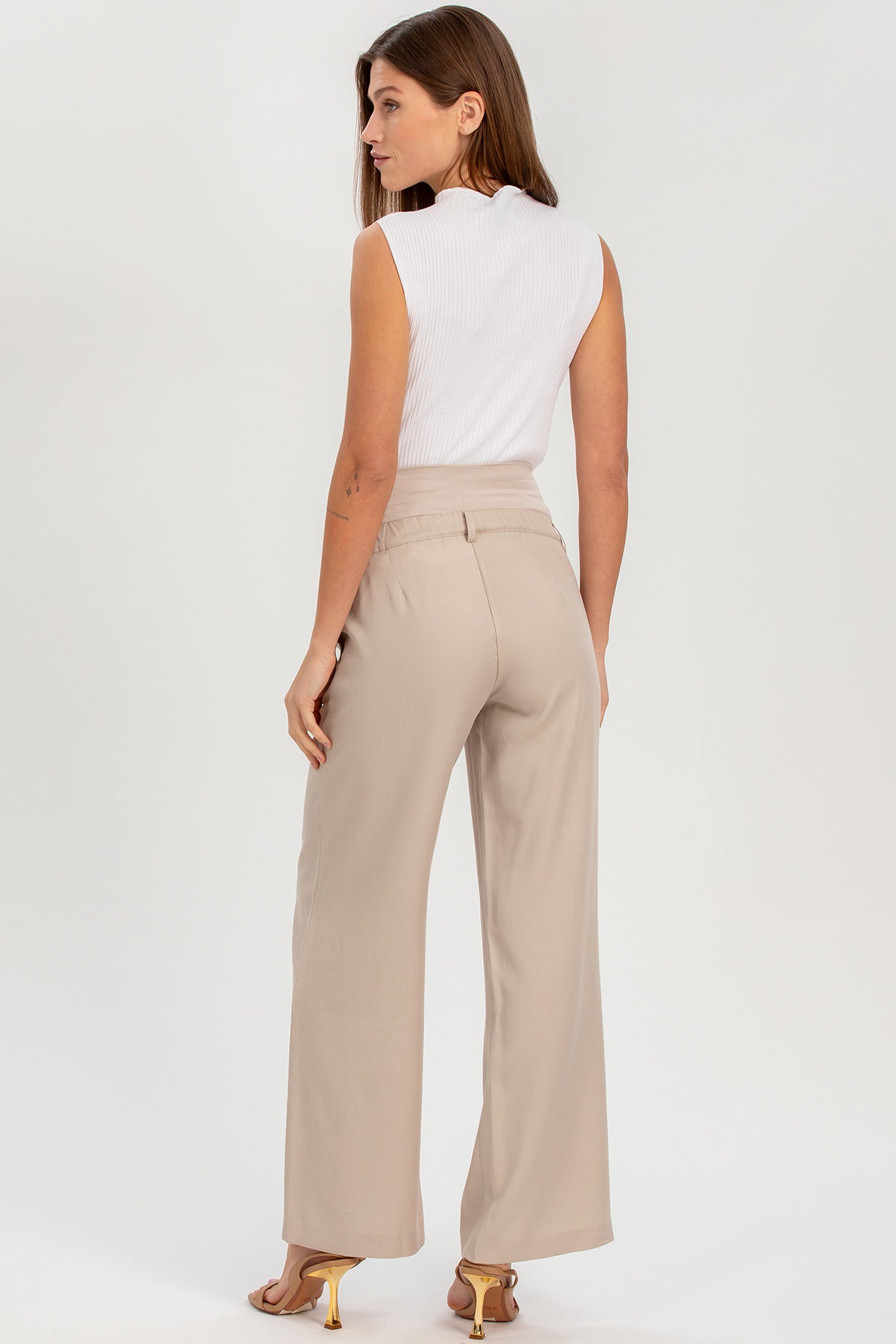Donna in pantaloni premaman beige a gamba larga e top smanicato bianco, vista da dietro