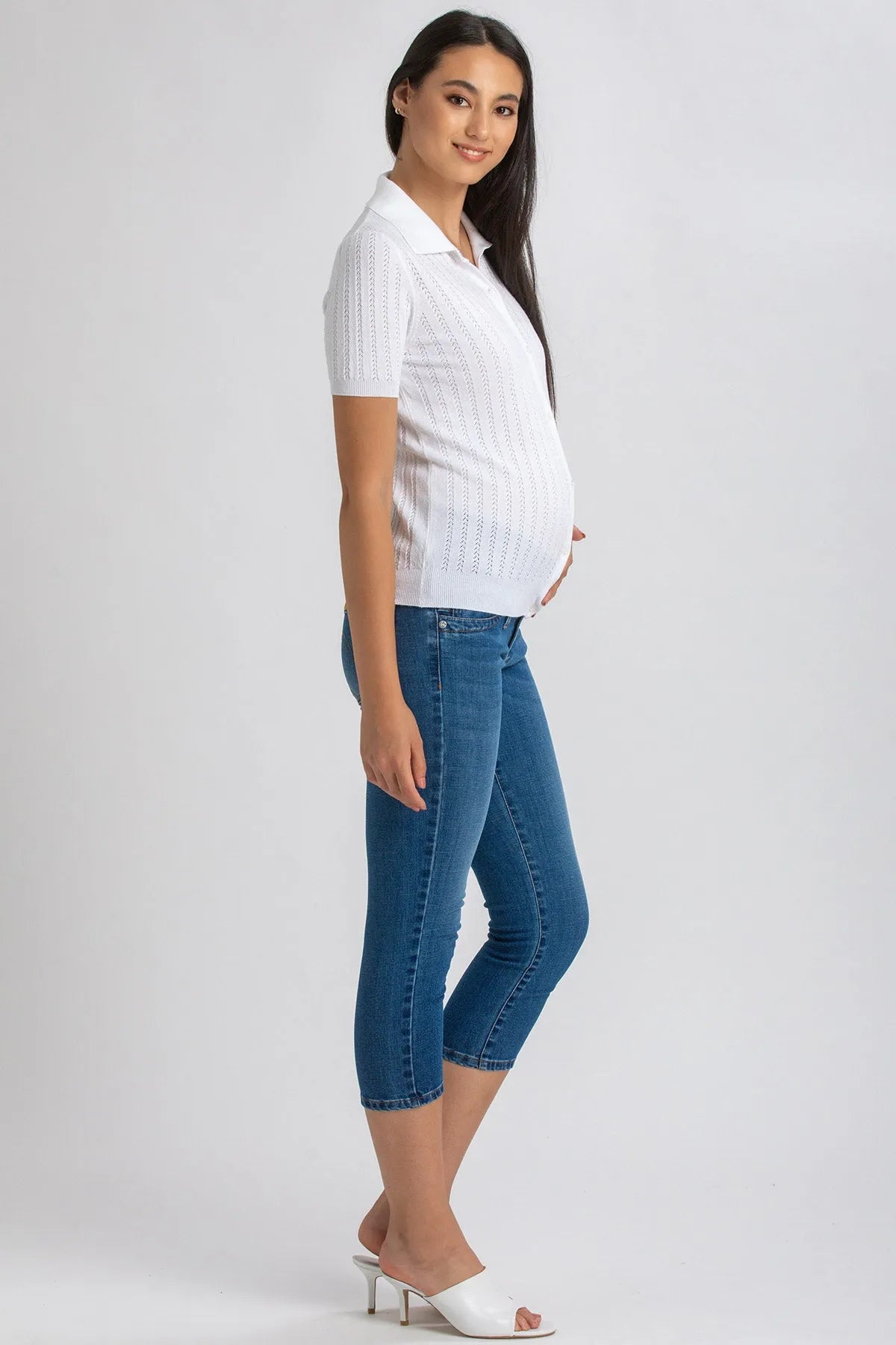 Modella incinta con jeans skinny premaman blu e maglia bianca a maniche corte