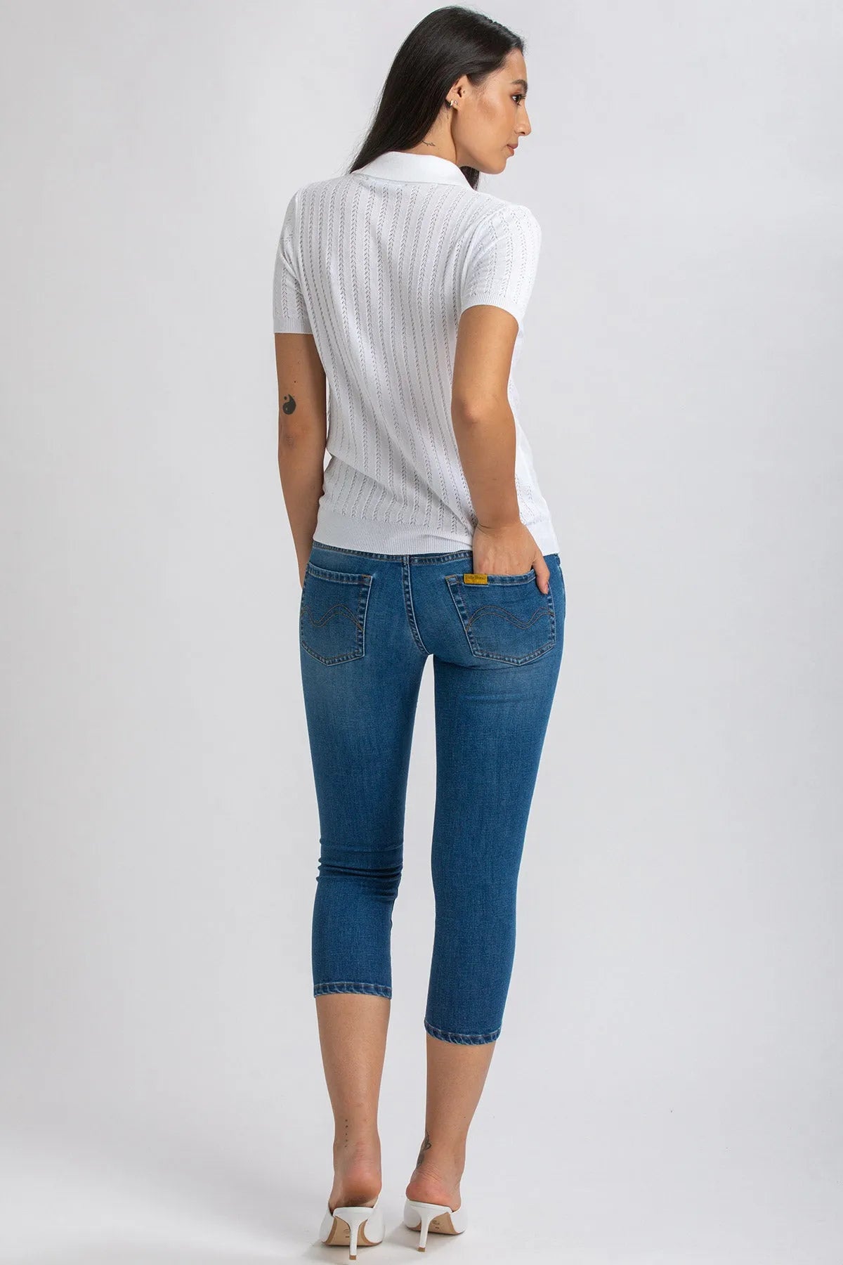 Donna di schiena con jeans premaman Capri skinny blu e maglia bianca, fondo neutro