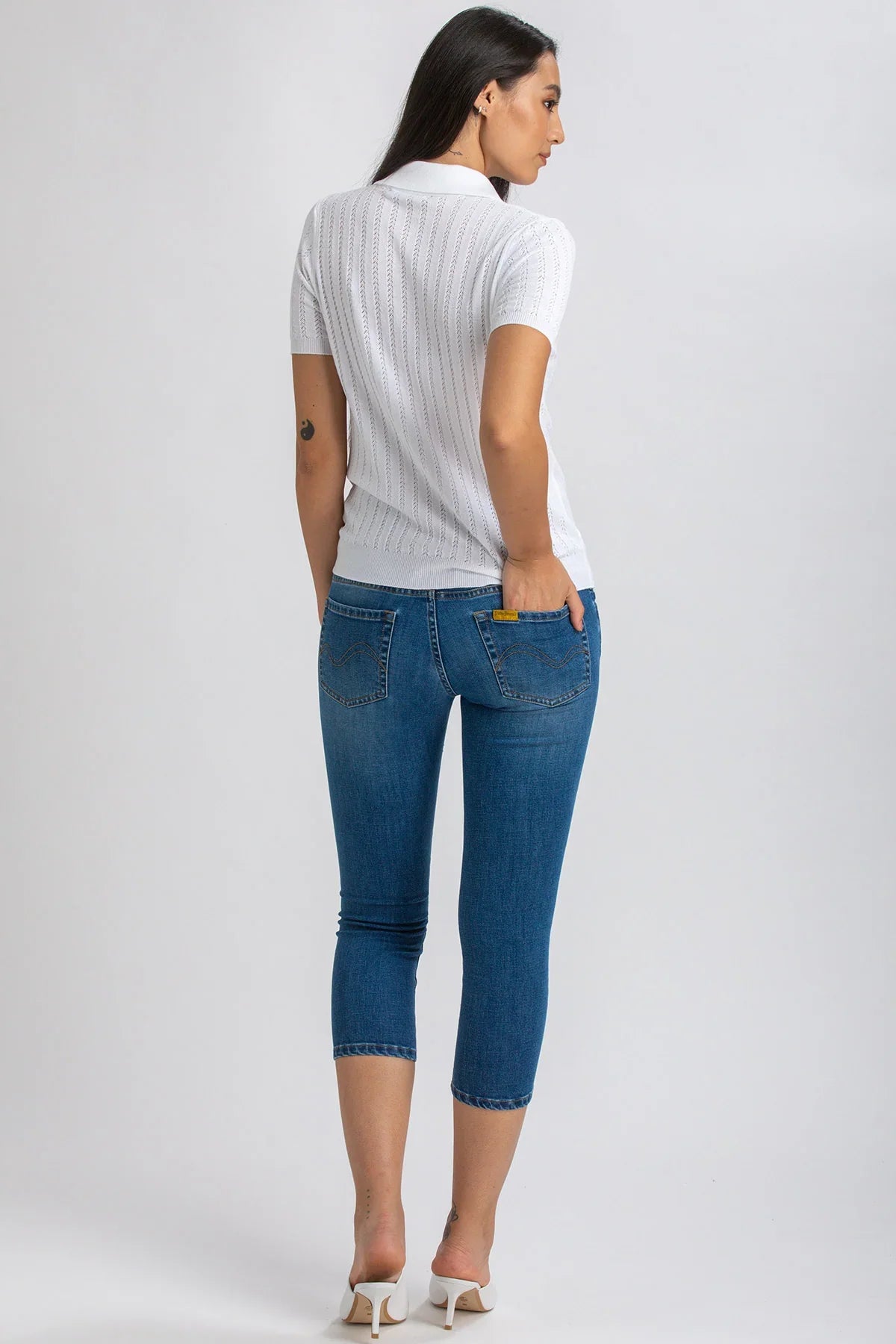 Donna di schiena con jeans premaman Capri skinny blu e maglia bianca, fondo neutro