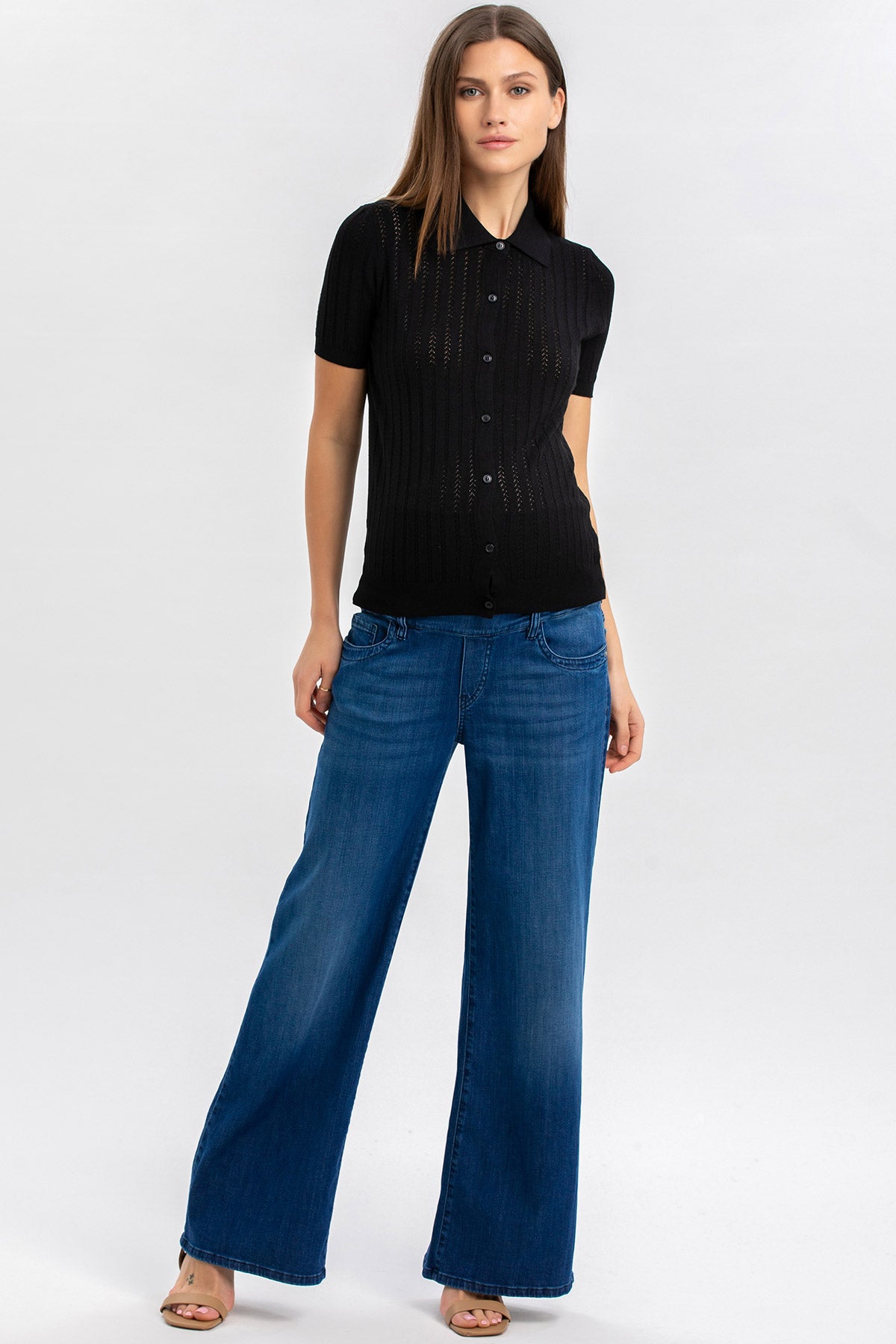 Donna con camicia nera a maniche corte e jeans premaman a gamba larga su sfondo chiaro