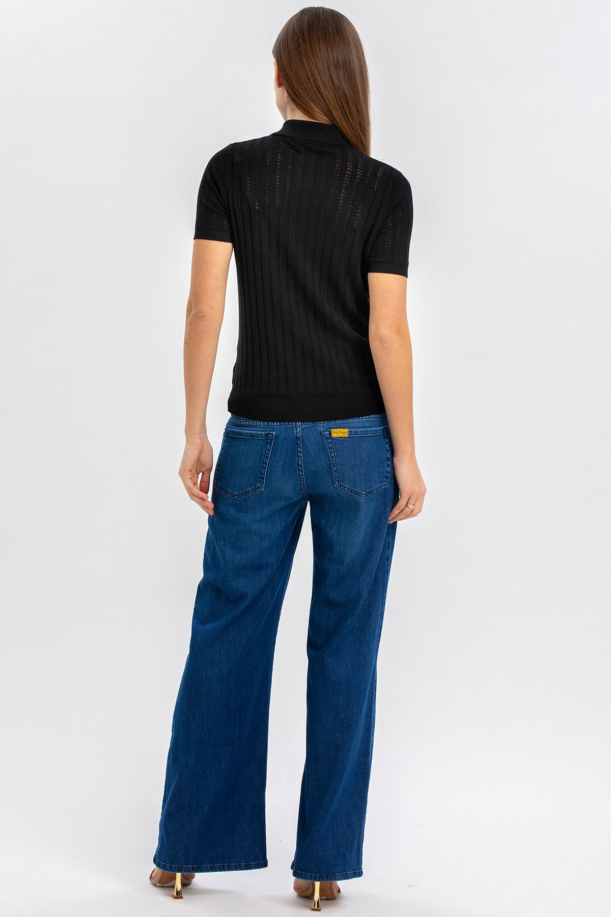 Donna di spalle con maglia nera a maniche corte e jeans premaman blu a gamba larga