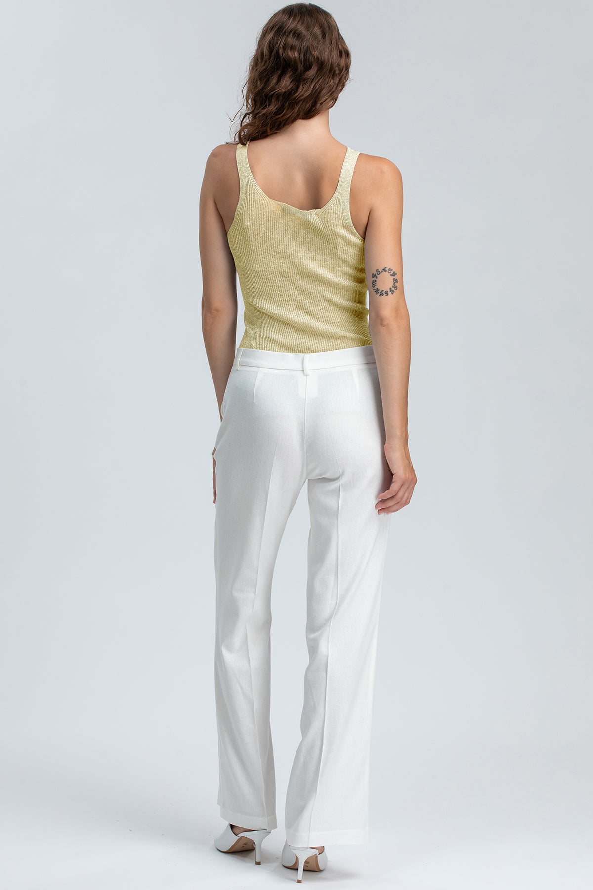 Donna di schiena indossa pantaloni premaman bianchi eleganti e top smanicato chiaro