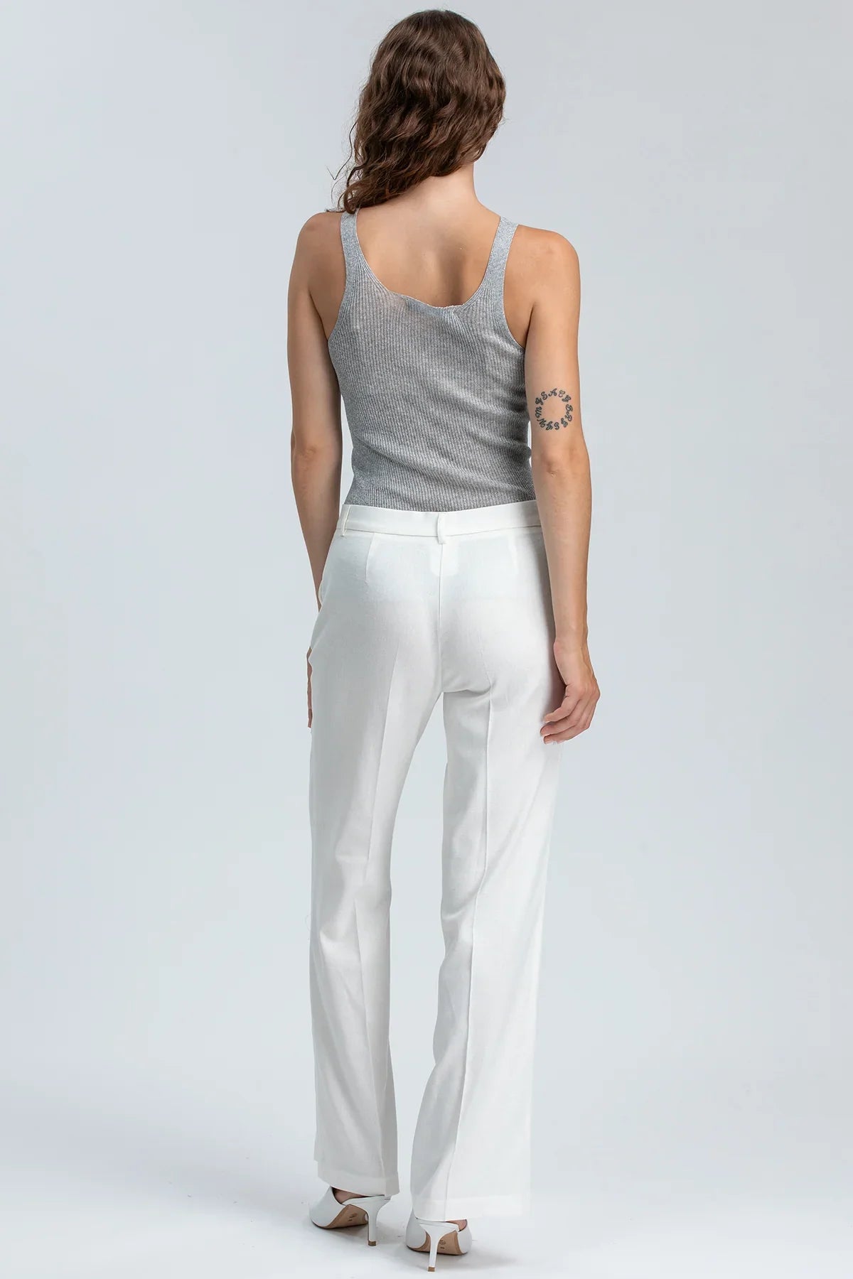 Donna di spalle con pantaloni premaman bianchi eleganti e top grigio, moda premaman elegante.
