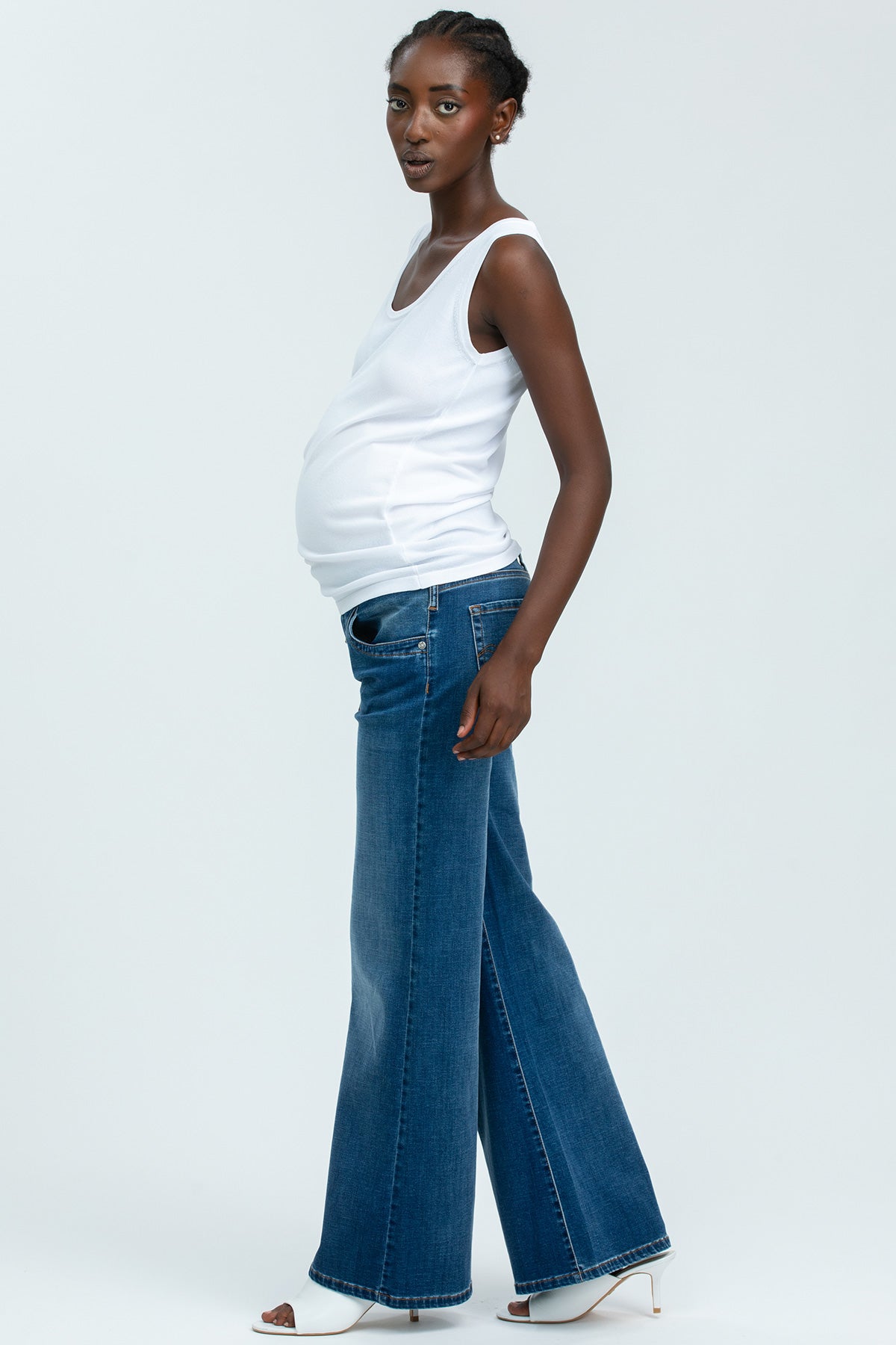 Donna incinta indossa top bianco premaman e jeans a gamba larga, stile moderno su sfondo neutro.