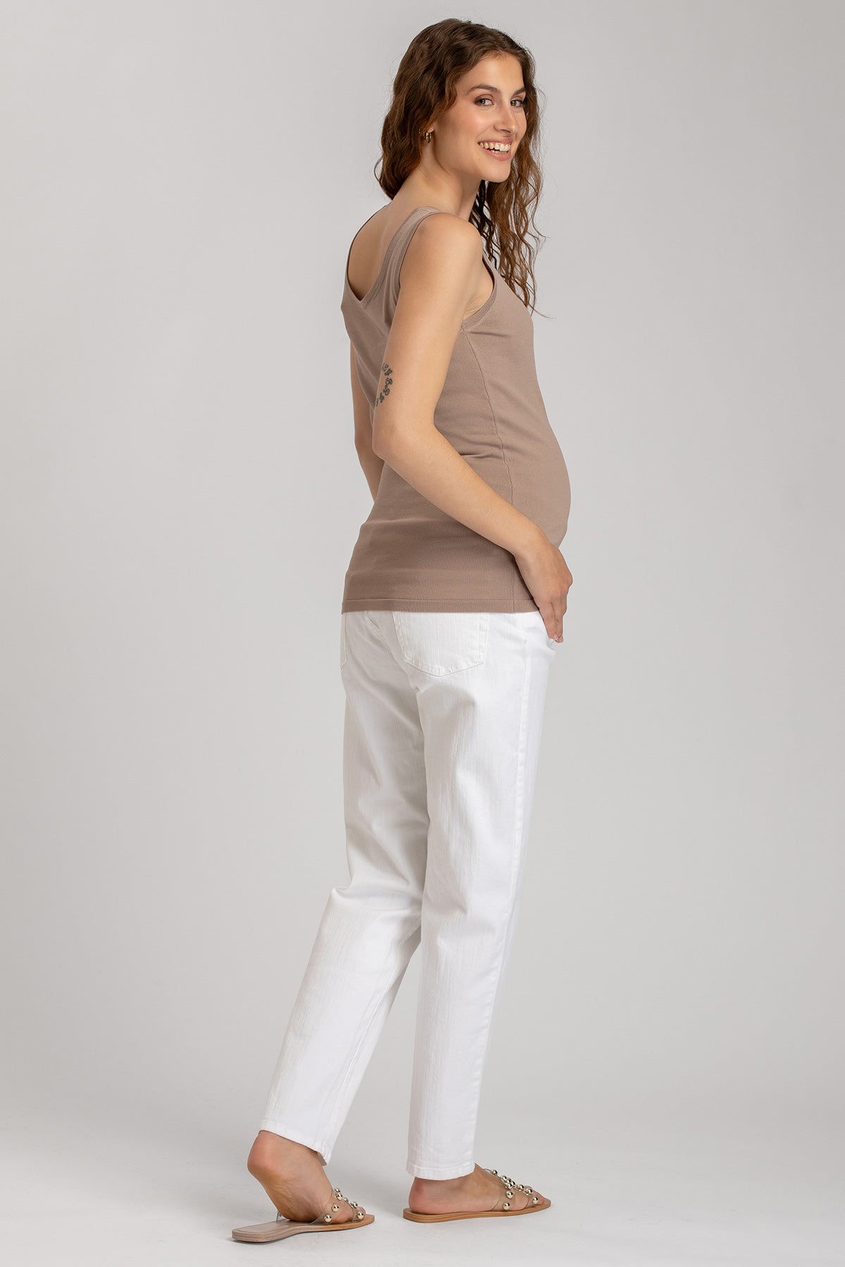 Donna incinta indossa top premaman beige e pantaloni premaman bianchi, outfit casual