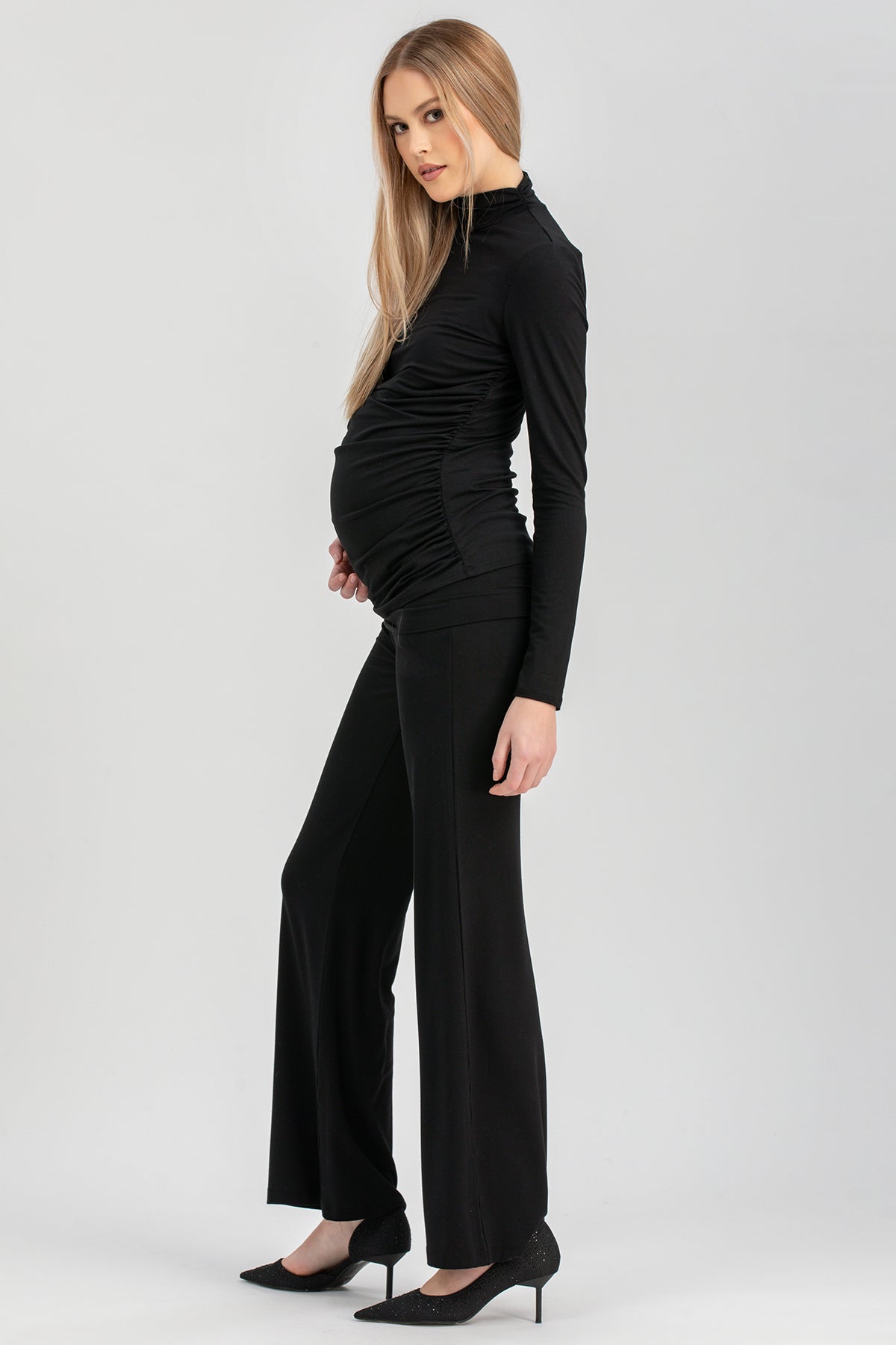 Modella premaman con pantaloni larghi e maglia nera eleganti, look sofisticato.