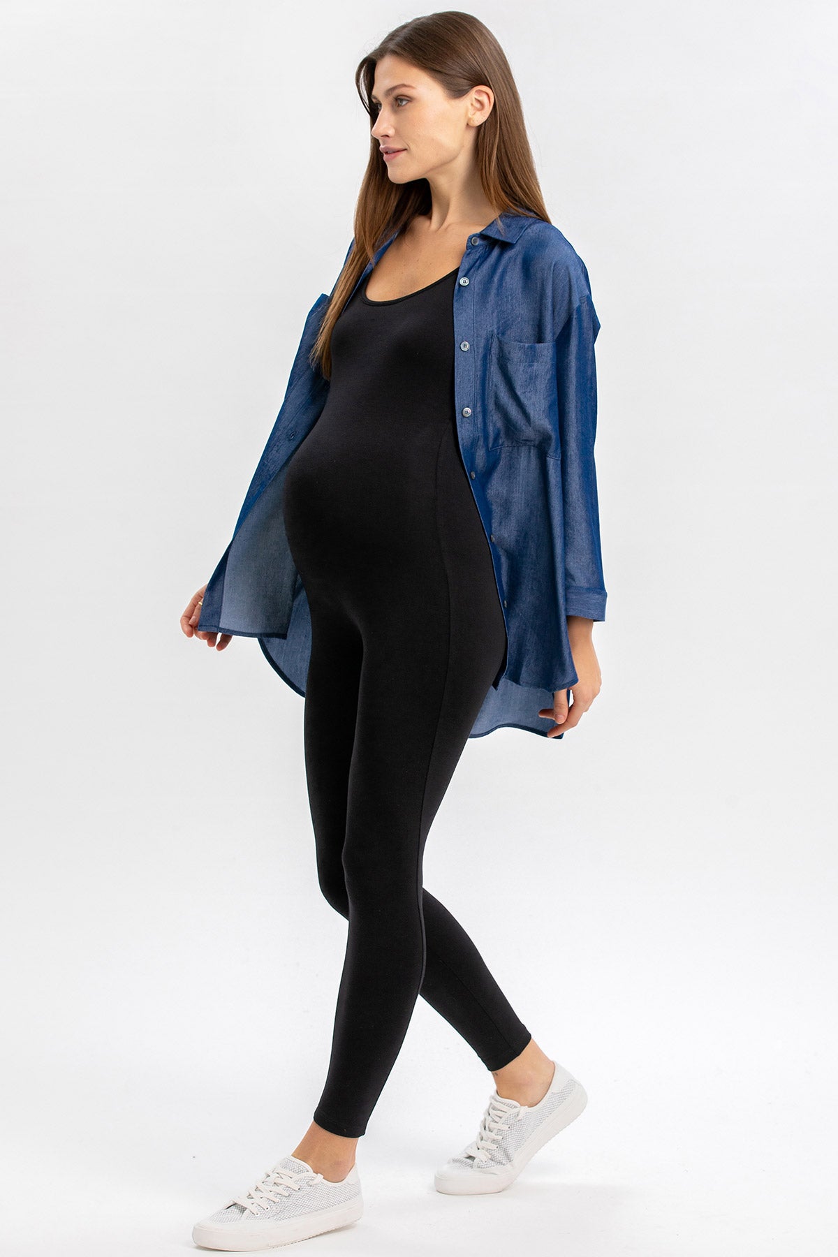Donna incinta con leggings premaman neri e camicia blu, stile casual.