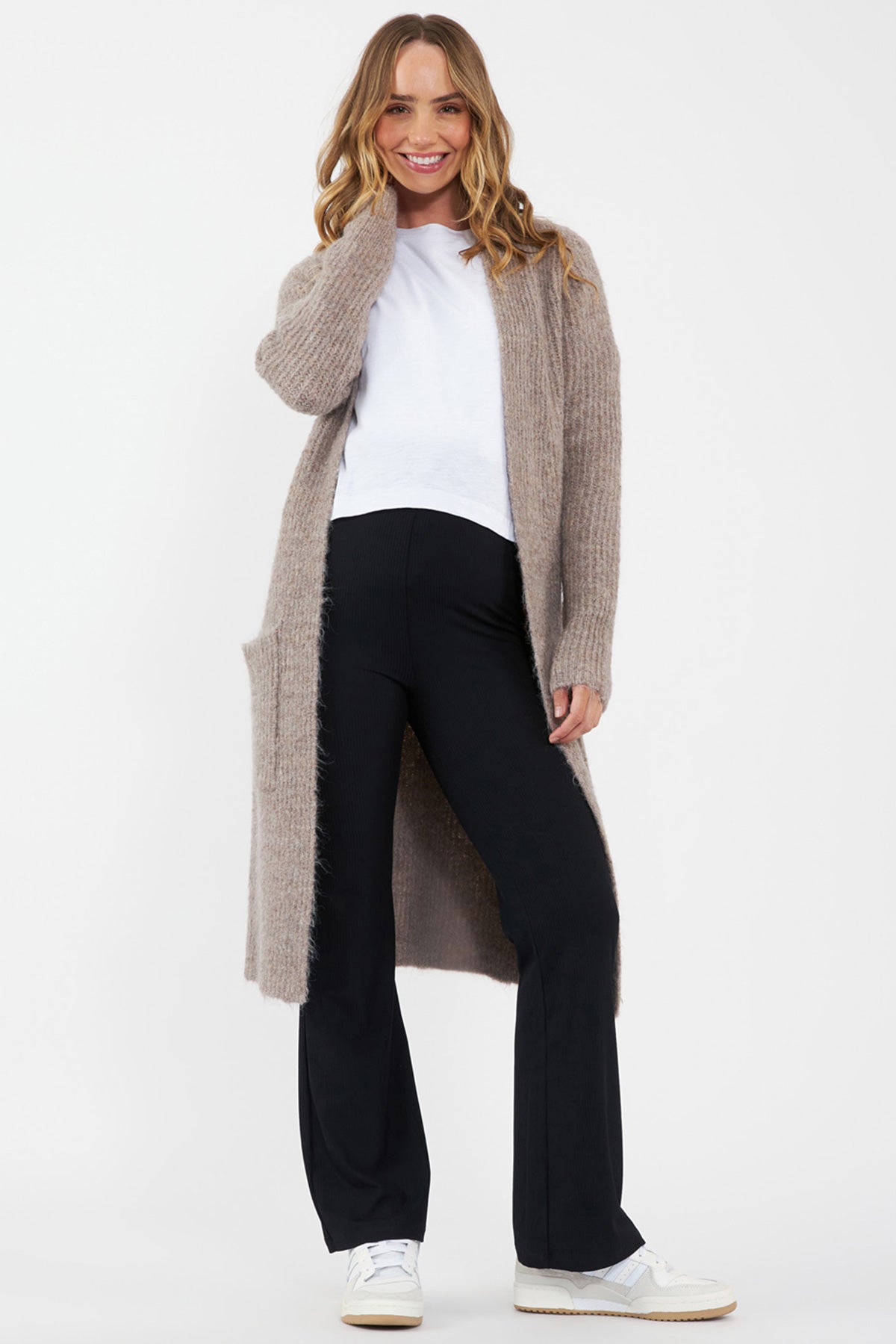 Donna con maglia premaman e allattamento bianca Ripe, cardigan beige e pantaloni premaman neri.