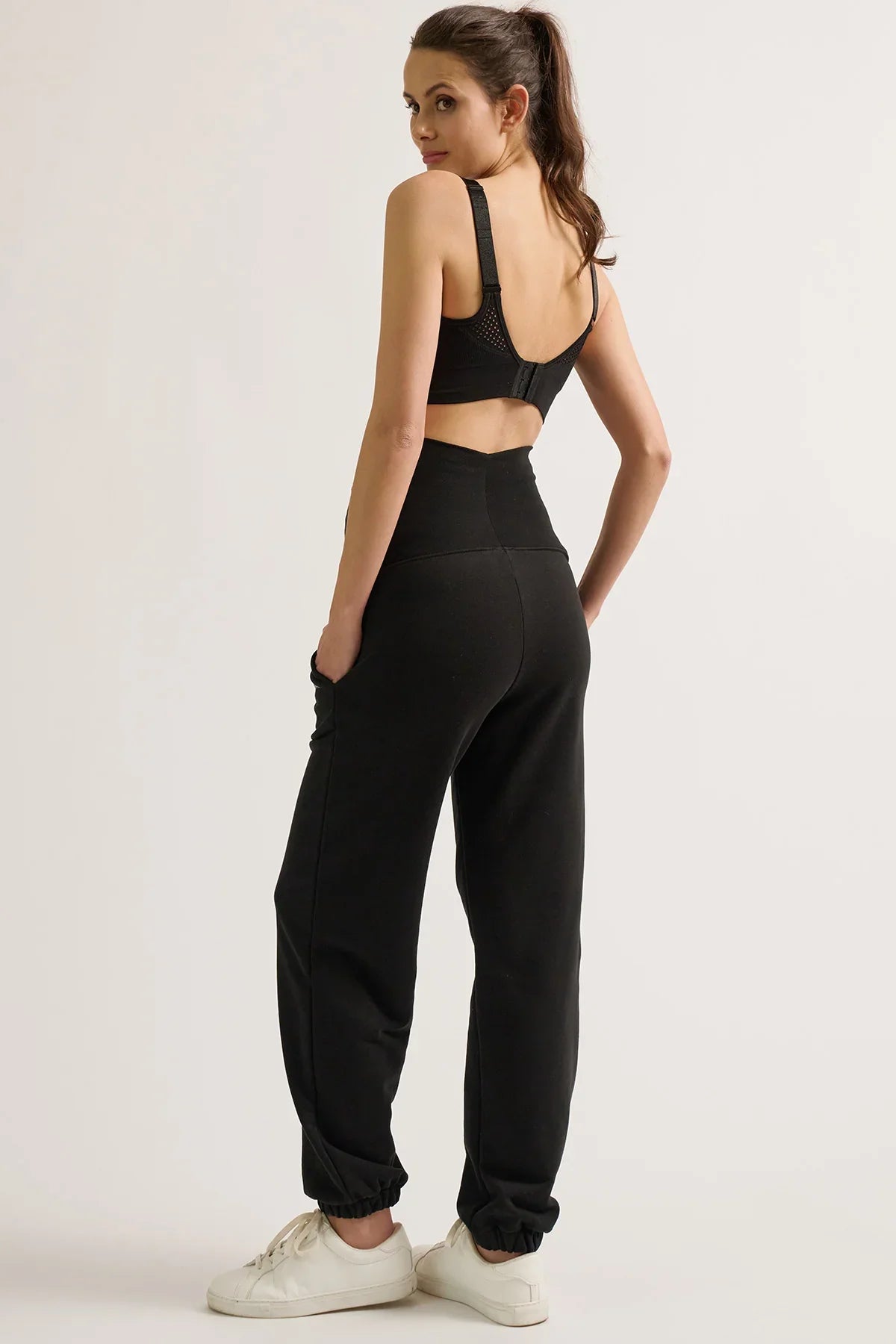 Donna di spalle con pantaloni jogger premaman neri Cache Coeur e reggiseno sportivo.