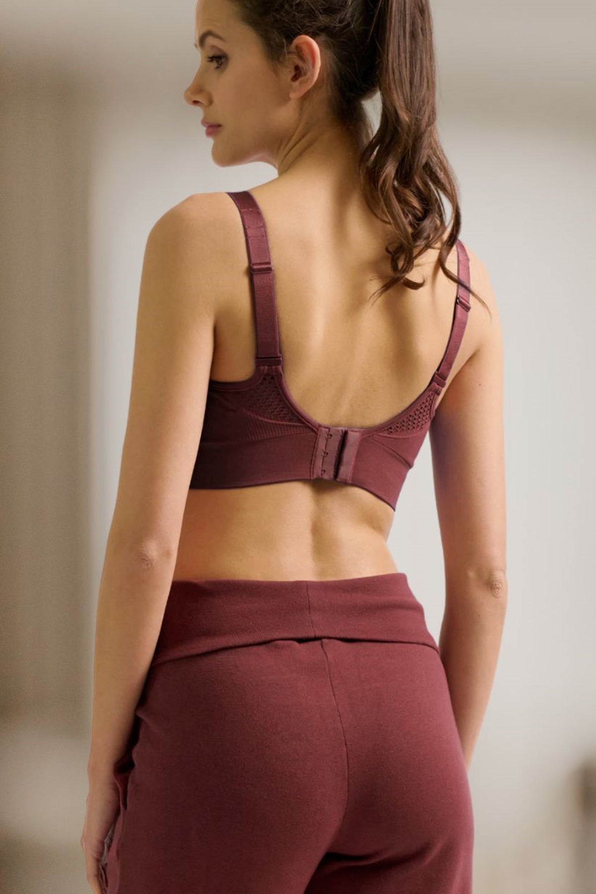 Donna di profilo con reggiseno e pantaloni premaman bordeaux, abbigliamento premaman comodo