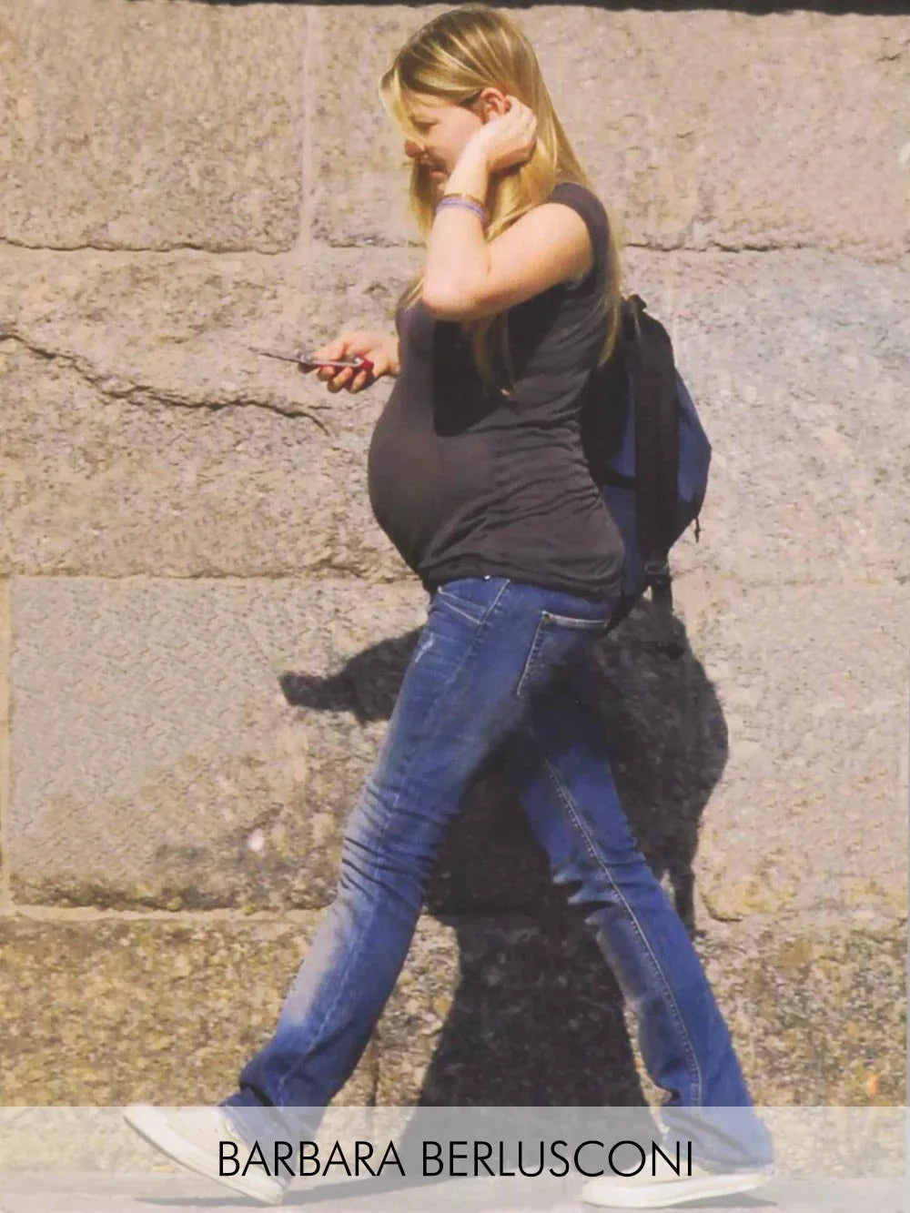 Donna con t-shirt nera e jeans premaman blu davanti a un muro di pietra.