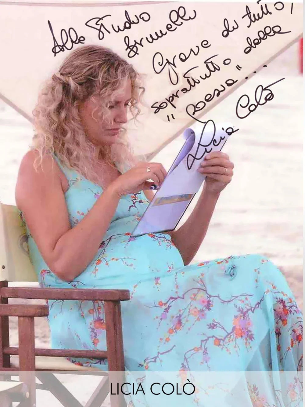 Donna con abito premaman azzurro a fiori che legge una rivista in spiaggia.
