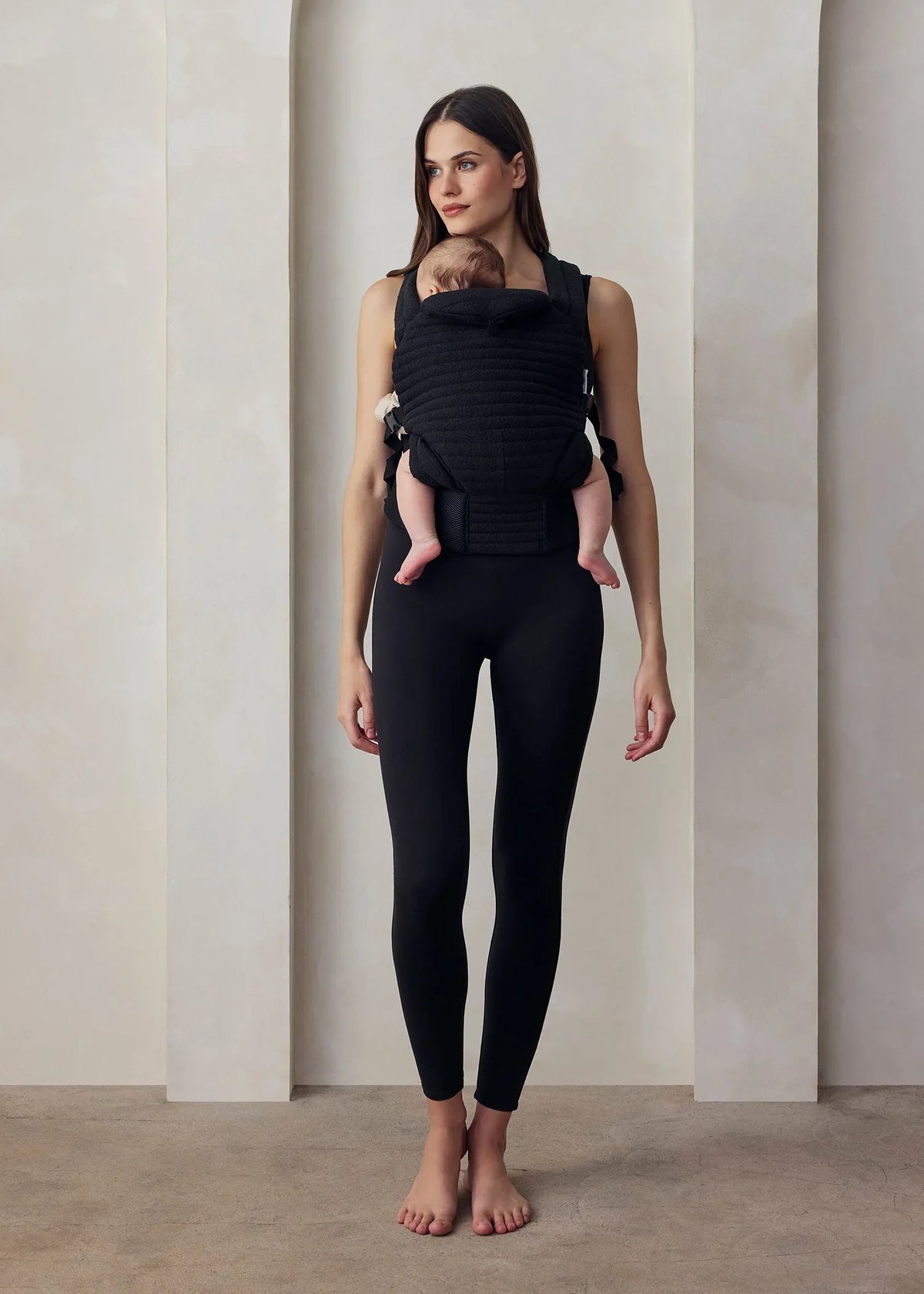 Donna con abbigliamento premaman nero e marsupio porta bebè, ambiente minimal