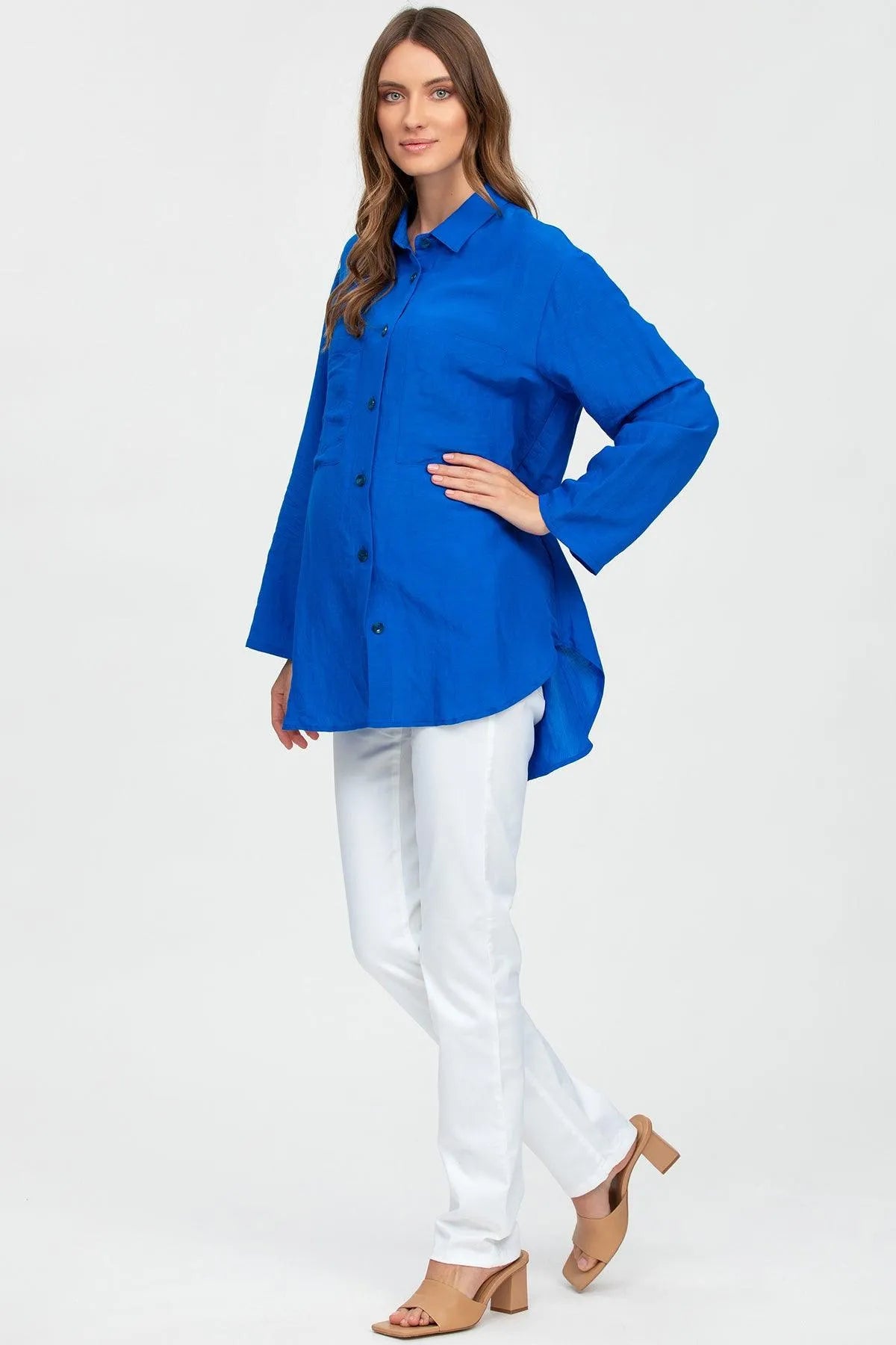 Donna premaman indossa camicia blu lunga e pantaloni bianchi, moda gravidanza elegante.
