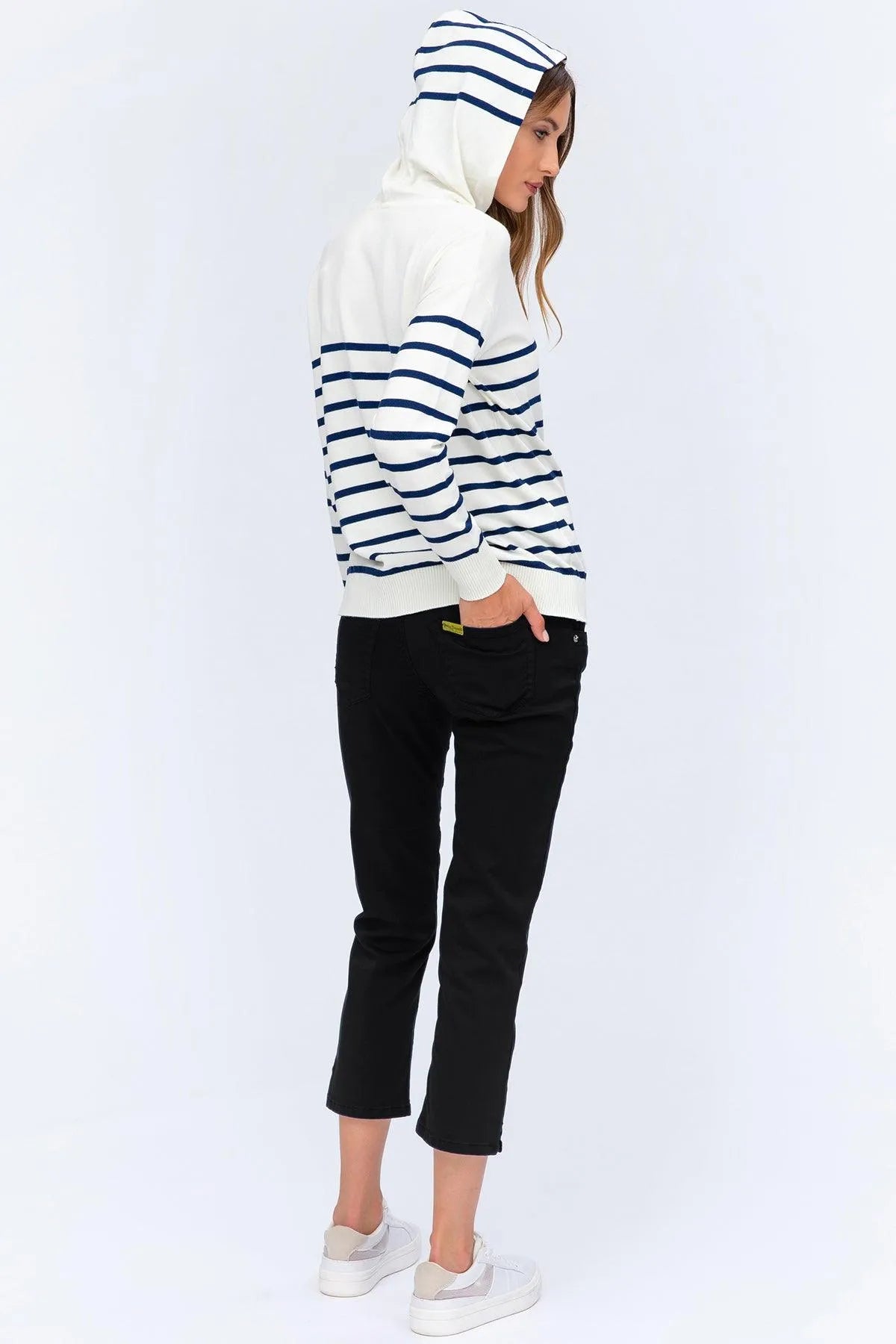 Donna con felpa premaman a righe bianche e blu, pantaloni neri e sneakers bianche