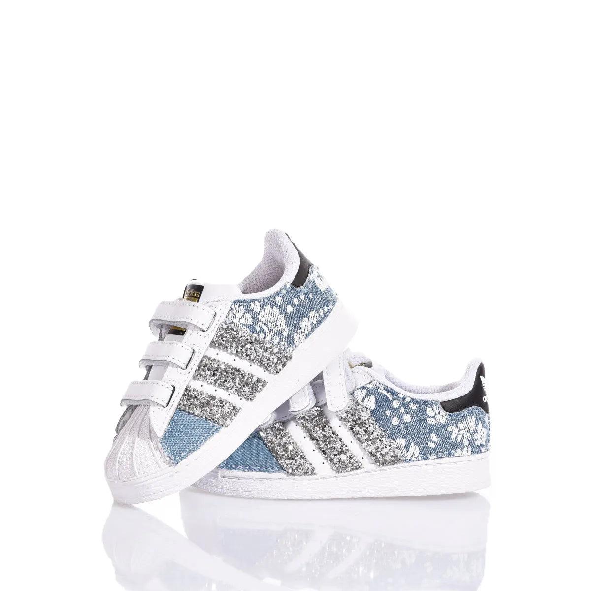 Scarpe da ginnastica bimbo con glitter argento, strappi e dettagli floreali bianchi su fondo azzurro