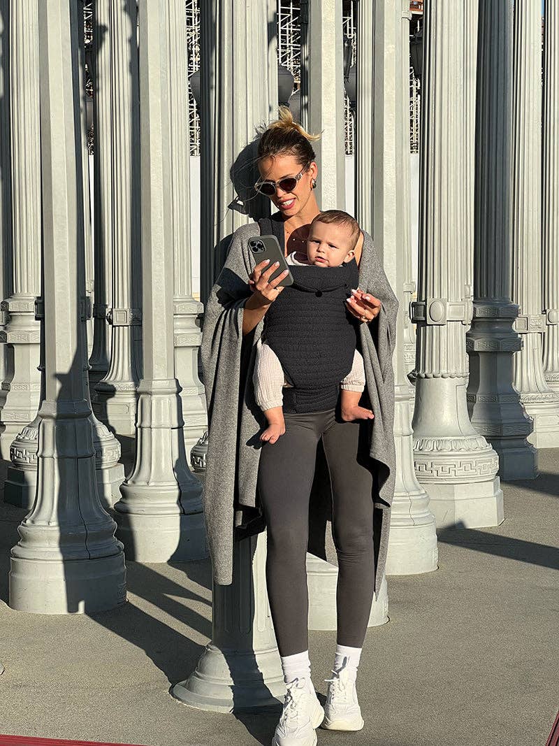 Donna con abbigliamento premaman moderno e bimbo in fascia davanti a colonne urbane