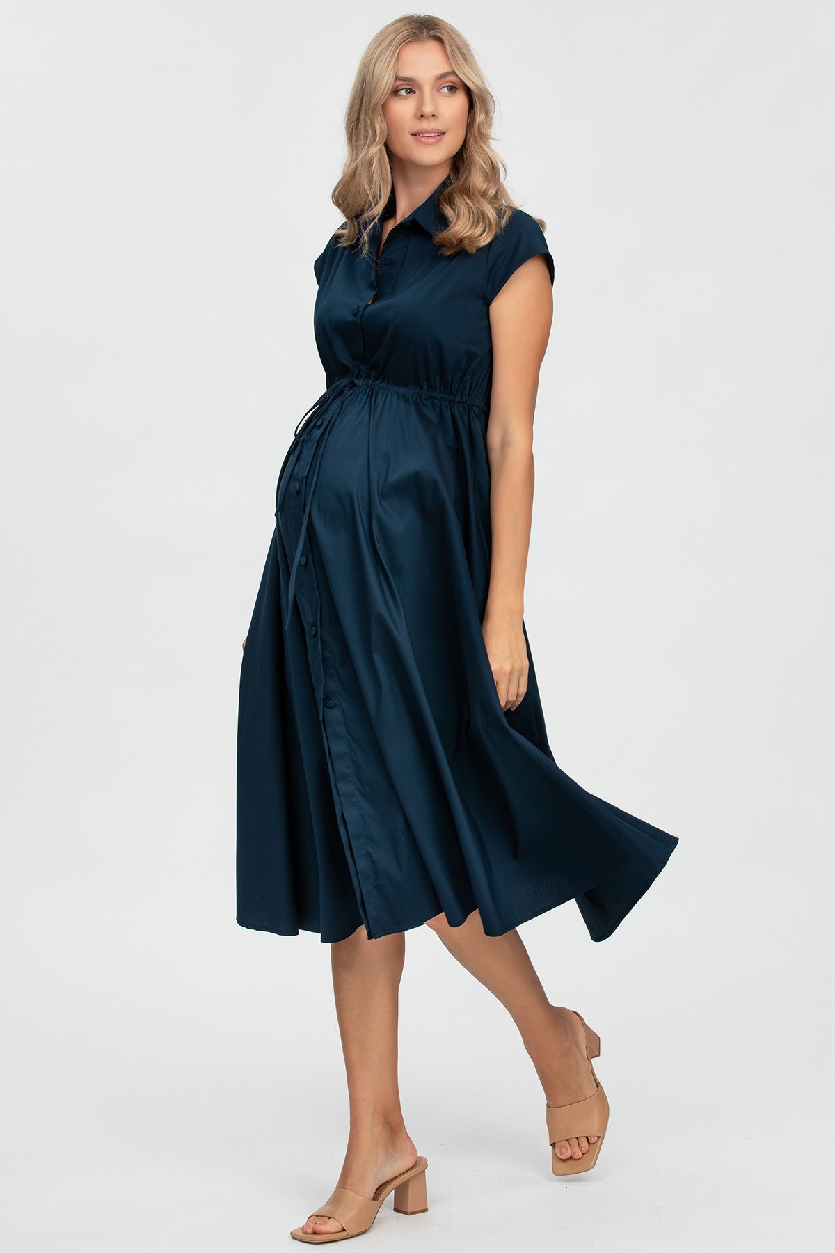 Abito premaman blu elegante a maniche corte, con bottoni e cintura sottoseno, indossato da donna incinta.