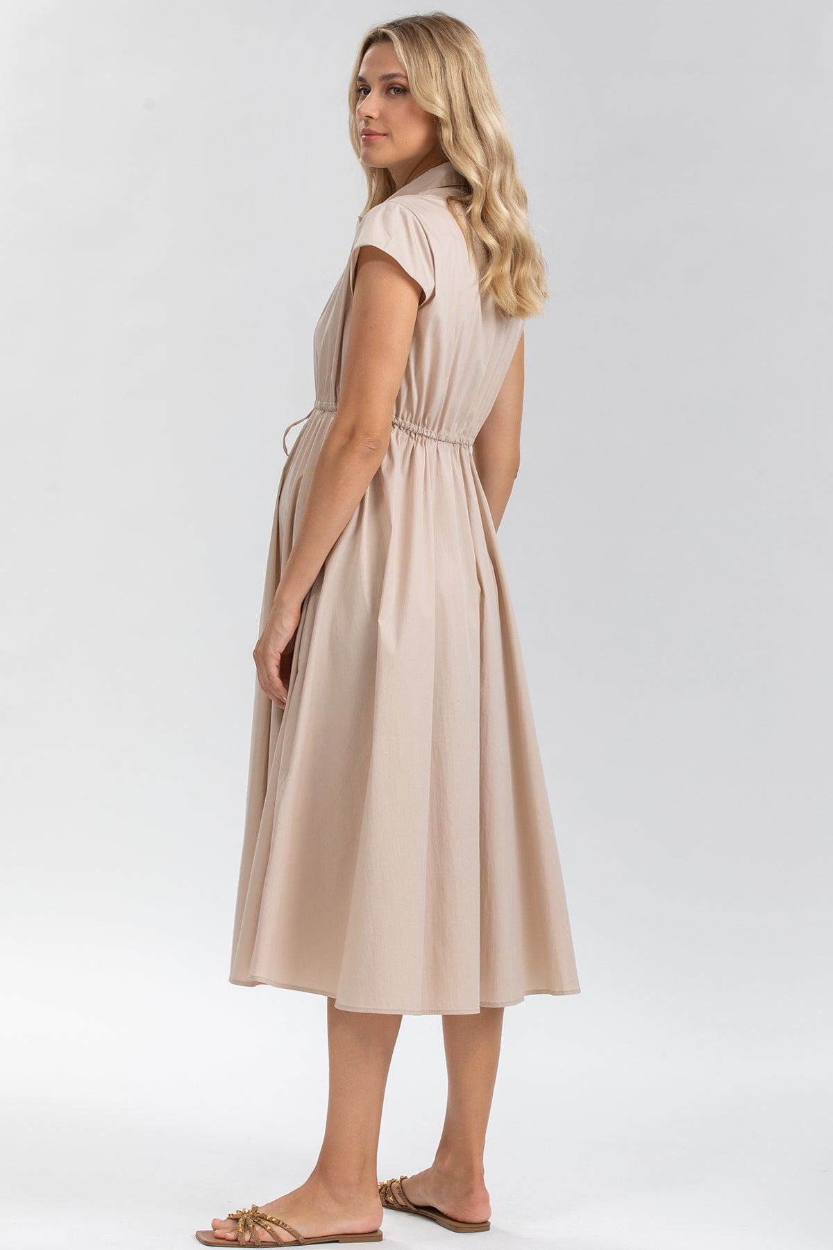 Donna con abito premaman beige a maniche corte, tessuto leggero, vista laterale.
