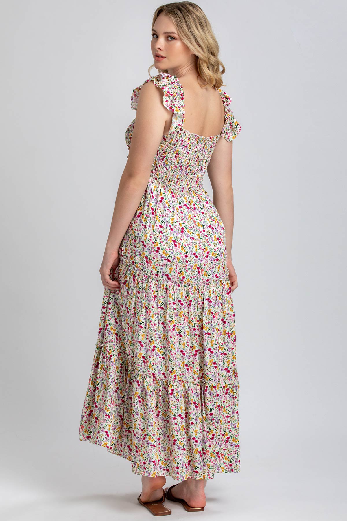 Donna con abito premaman lungo floreale, spalline a volant, sfondo neutro.