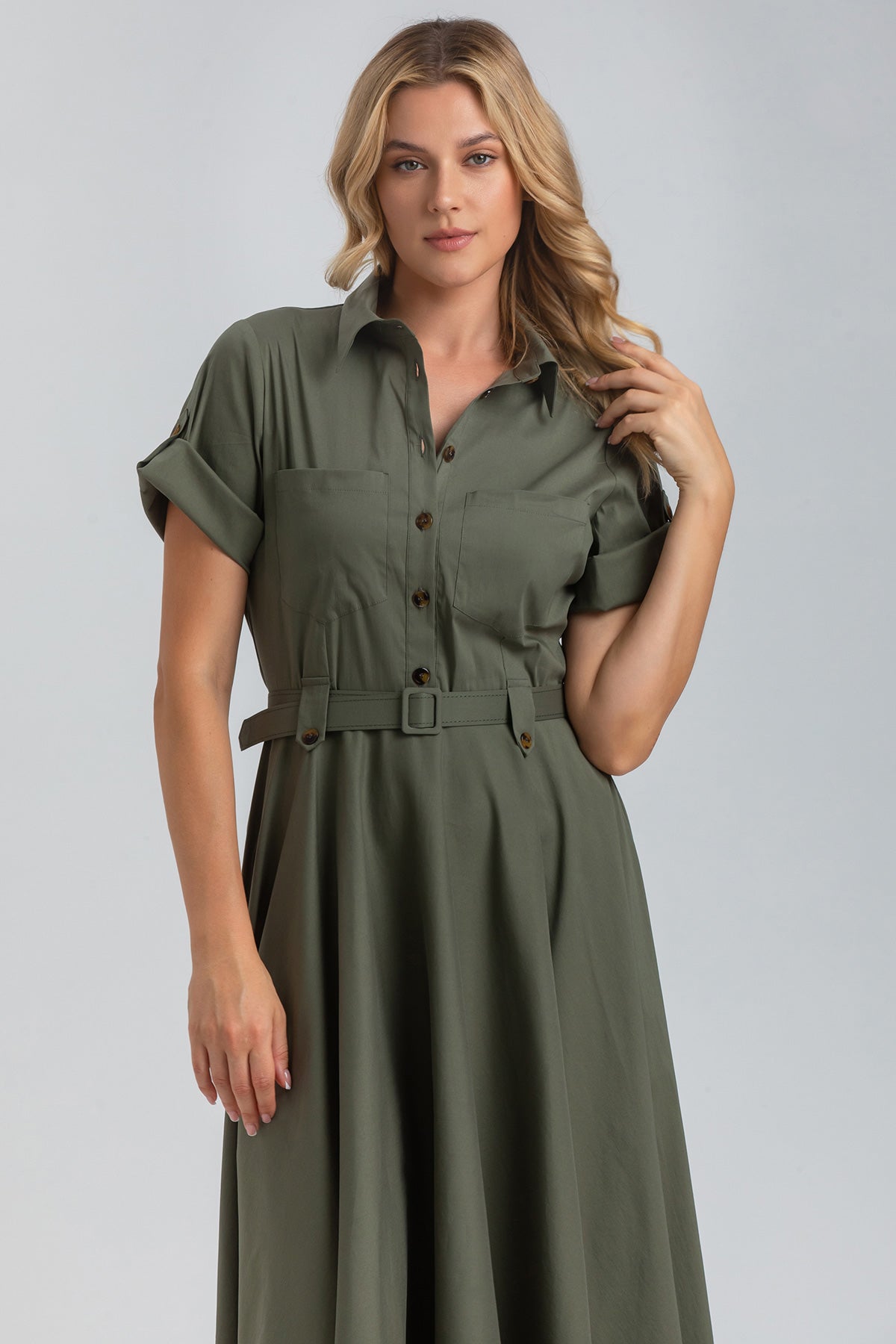 Abito premaman verde oliva con cintura, maniche risvoltate e bottoni, indossato da donna bionda.