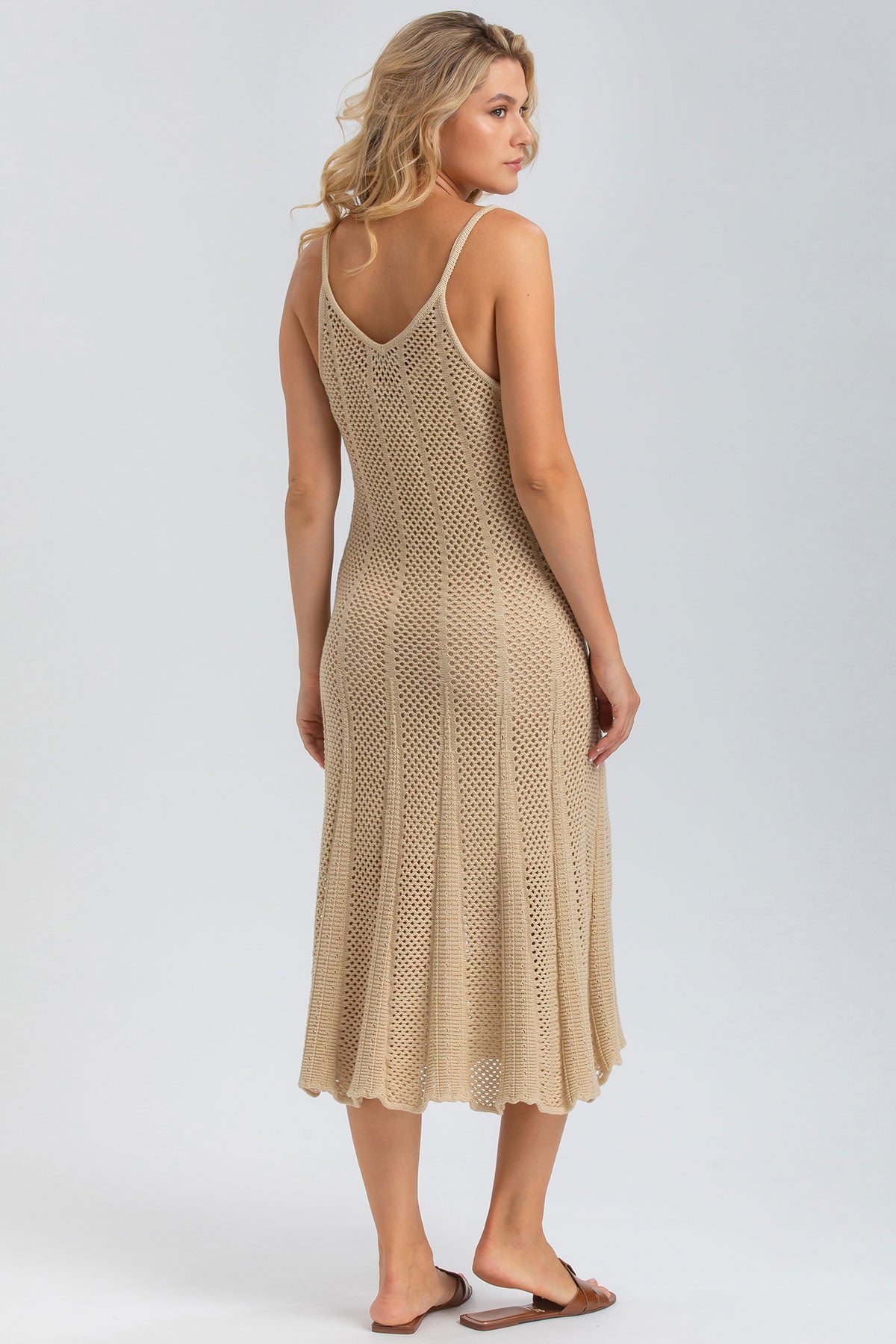 Donna di spalle con abito premaman beige in maglia traforata, sandali bassi