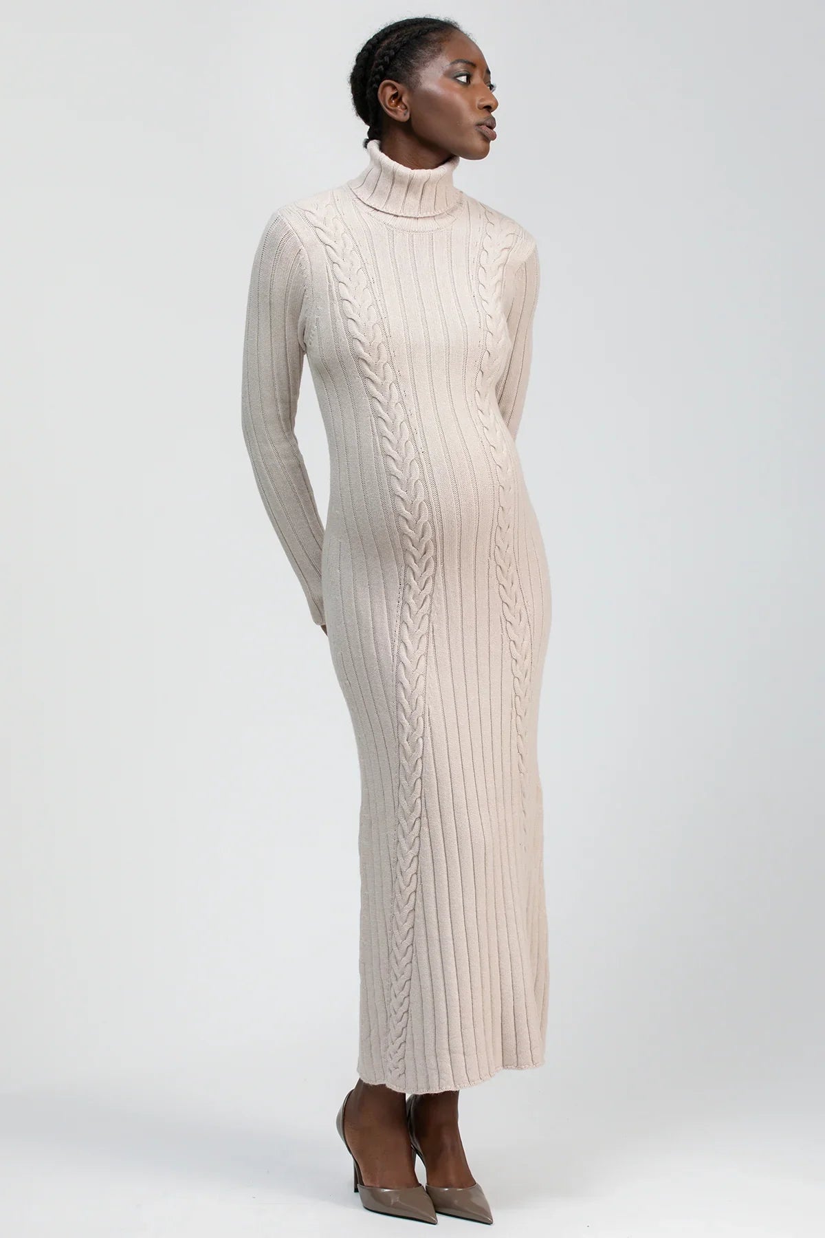 Abito premaman lungo a collo alto in maglia beige con lavorazione a trecce, donna in posa elegante.