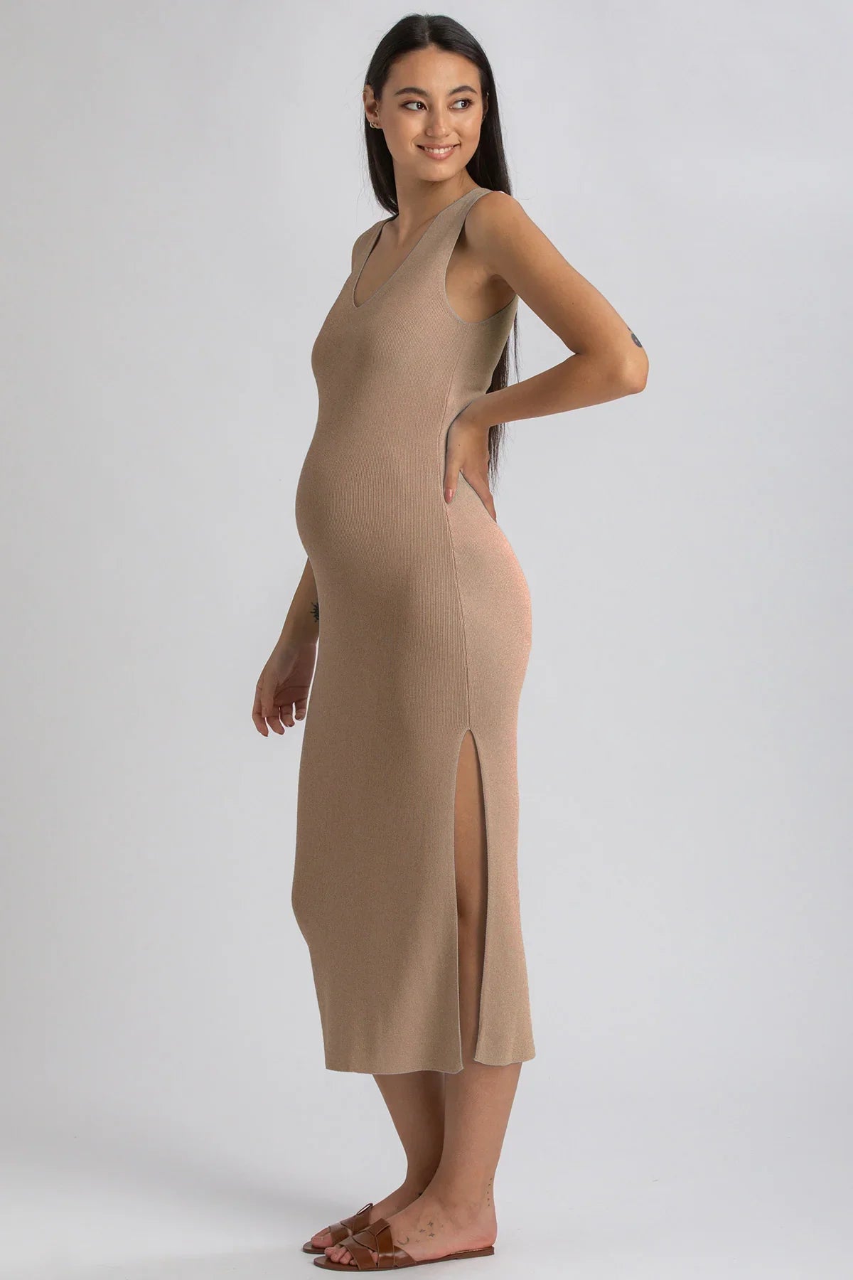Donna incinta con abito premaman beige senza maniche e spacco laterale, posa su sfondo neutro