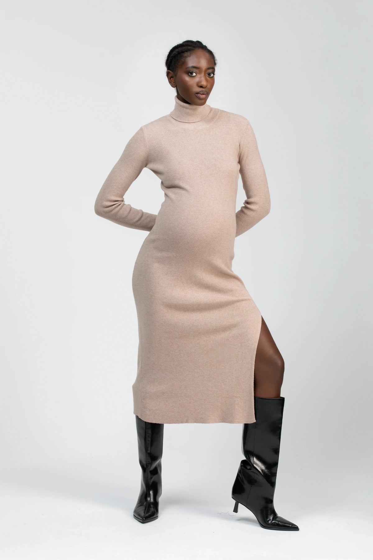 Donna incinta con abito premaman beige a collo alto e spacco laterale, stivali neri