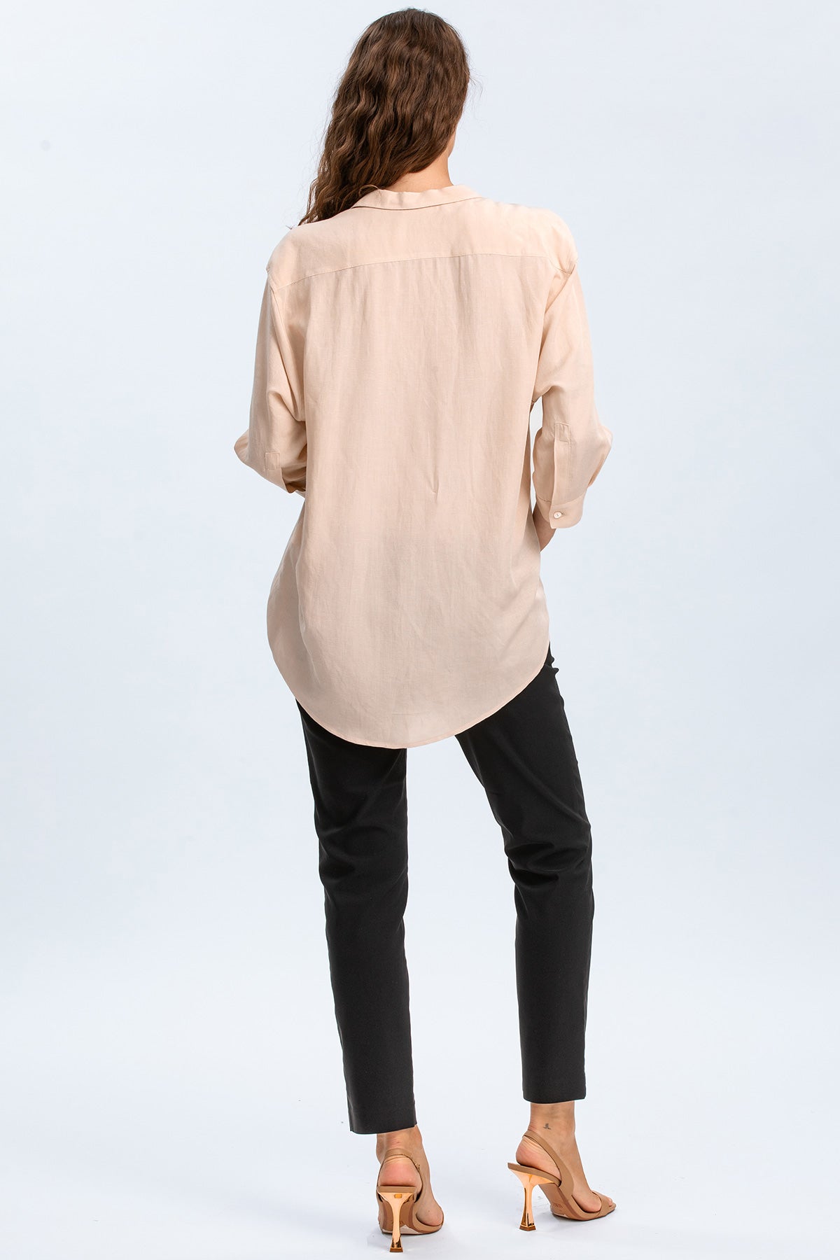 Donna di spalle con camicia premaman beige, pantaloni neri e sandali eleganti.