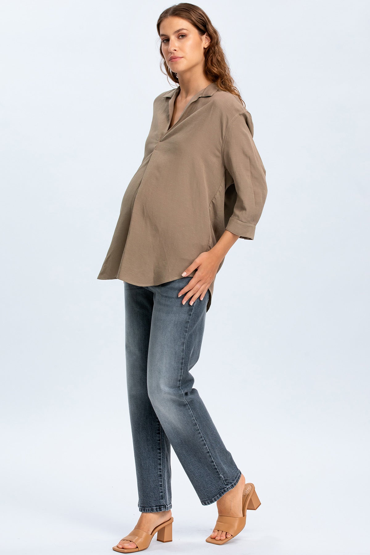 Modella incinta con camicia premaman beige e jeans premaman dritti, moda gravidanza elegante.