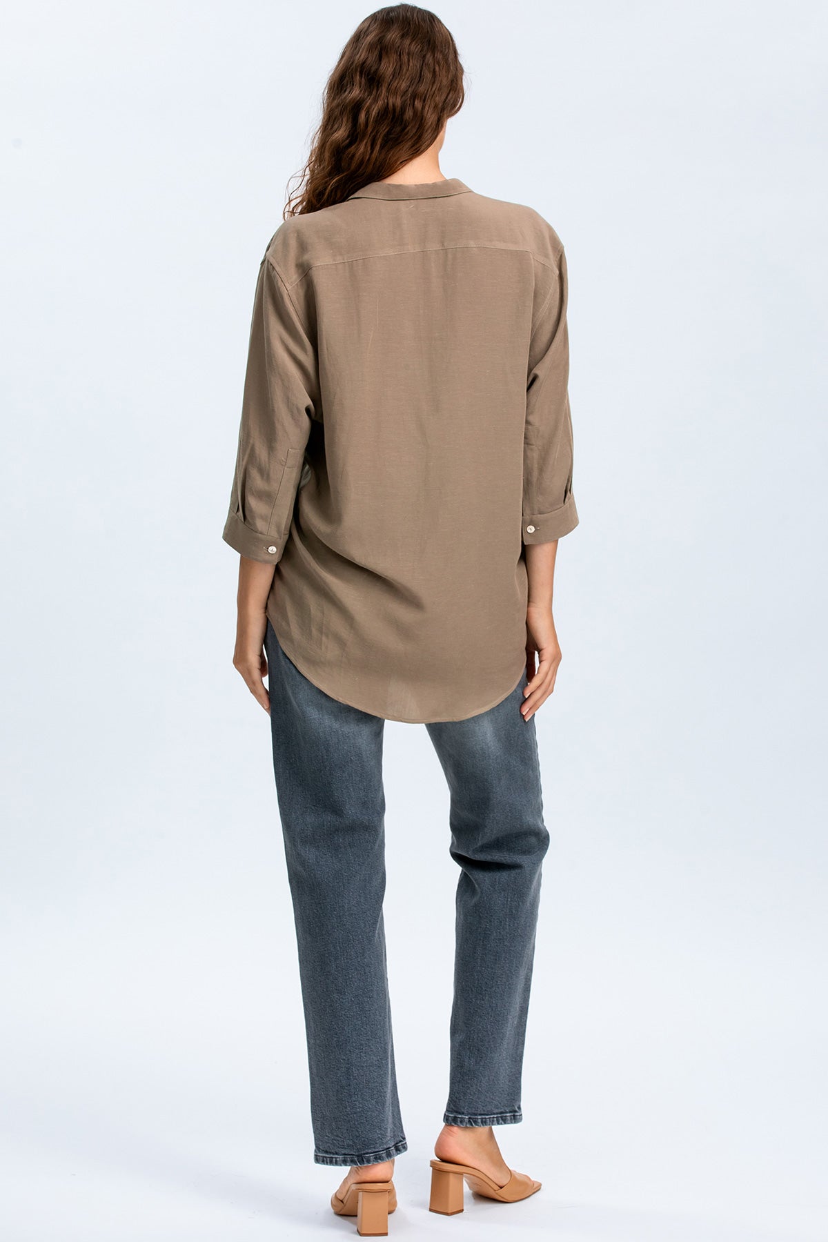 Donna di spalle con camicia premaman beige e jeans dritti, look abbigliamento gravidanza