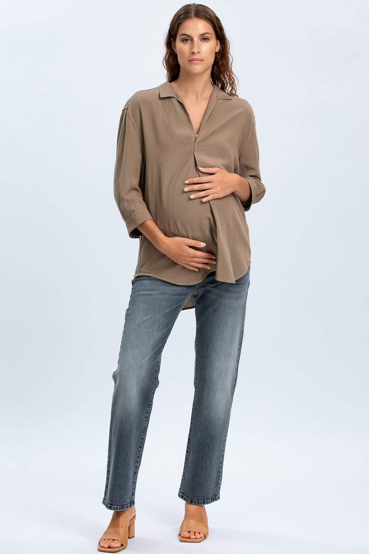 Modella premaman con camicia beige e jeans premaman dritti, posa studio, abbigliamento gravidanza