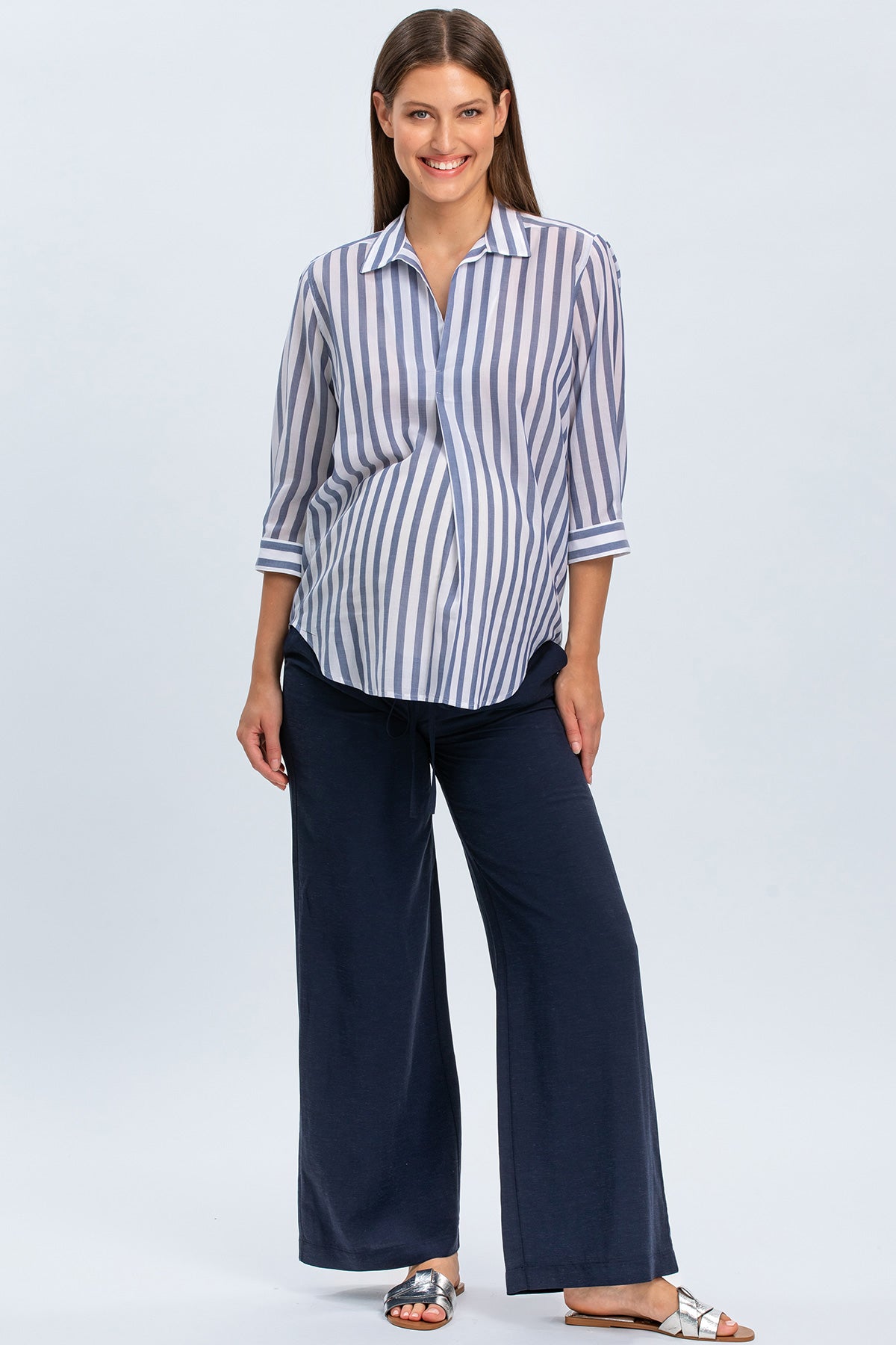 Donna incinta con camicia premaman a righe blu e pantaloni larghi navy in studio
