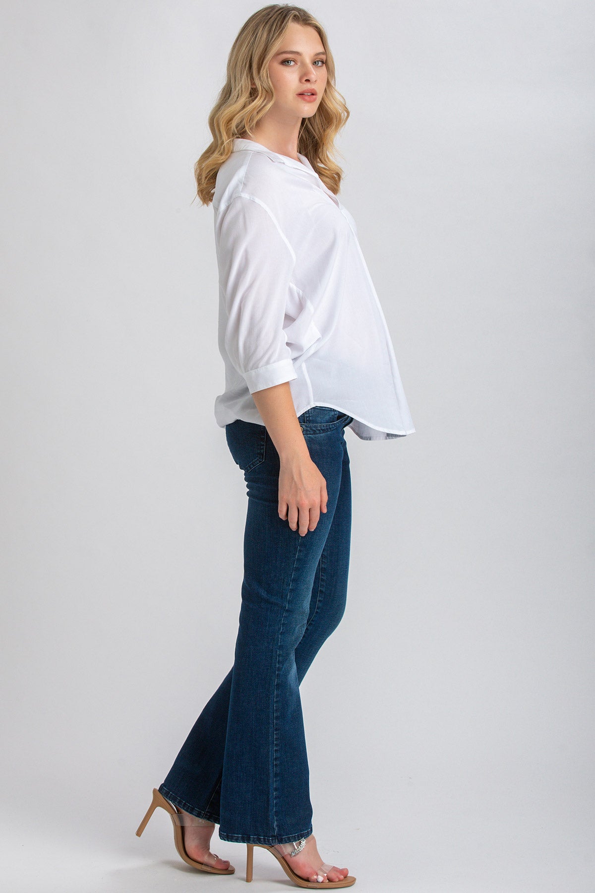 Donna in camicia bianca premaman e jeans flare blu, look casual elegante.