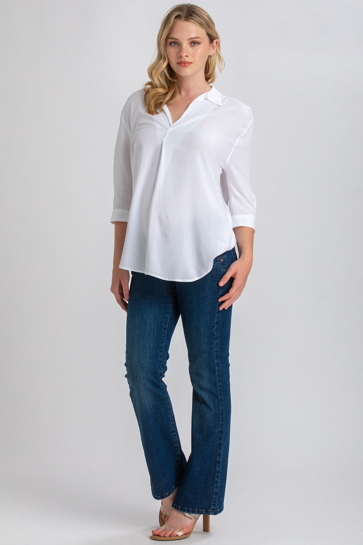 Donna con camicia premaman bianca a maniche lunghe e jeans flare blu, look casual elegante.