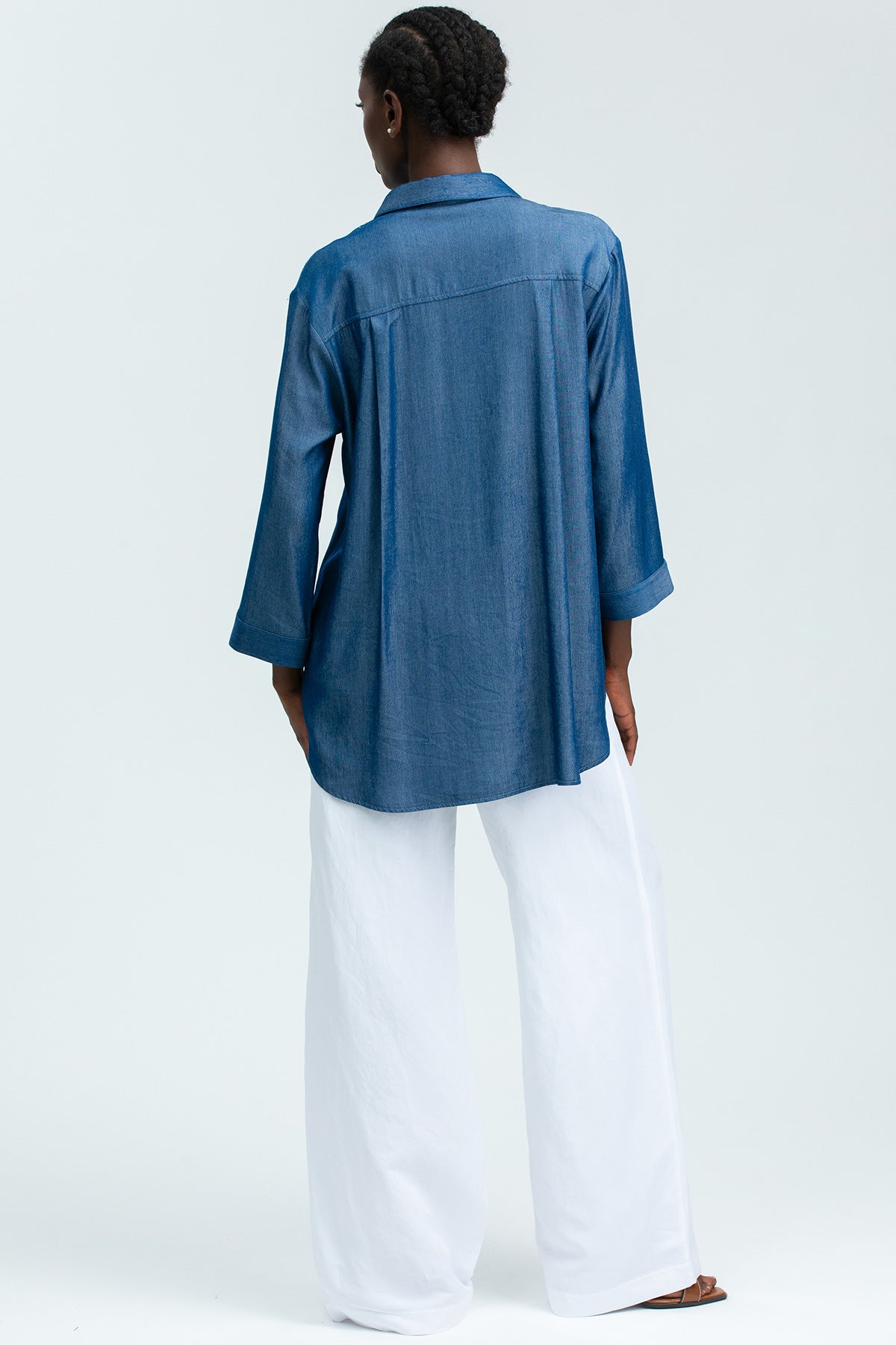 Donna di spalle con camicia premaman in denim blu e pantaloni larghi bianchi