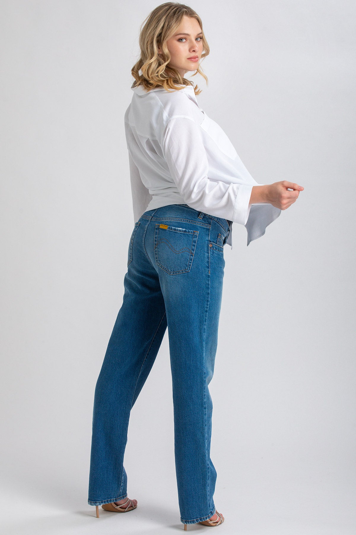Donna in camicia bianca e jeans premaman dritti in denim blu, posa su sfondo chiaro
