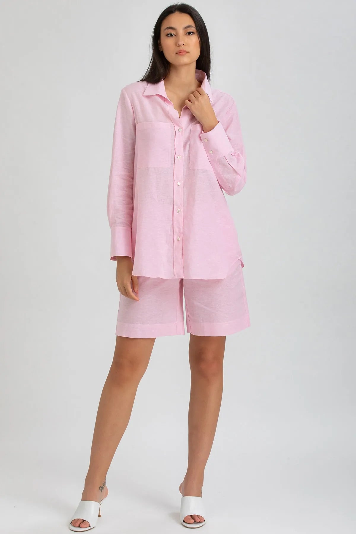 Donna con camicia premaman rosa a maniche lunghe e shorts coordinati in lino, su sfondo neutro